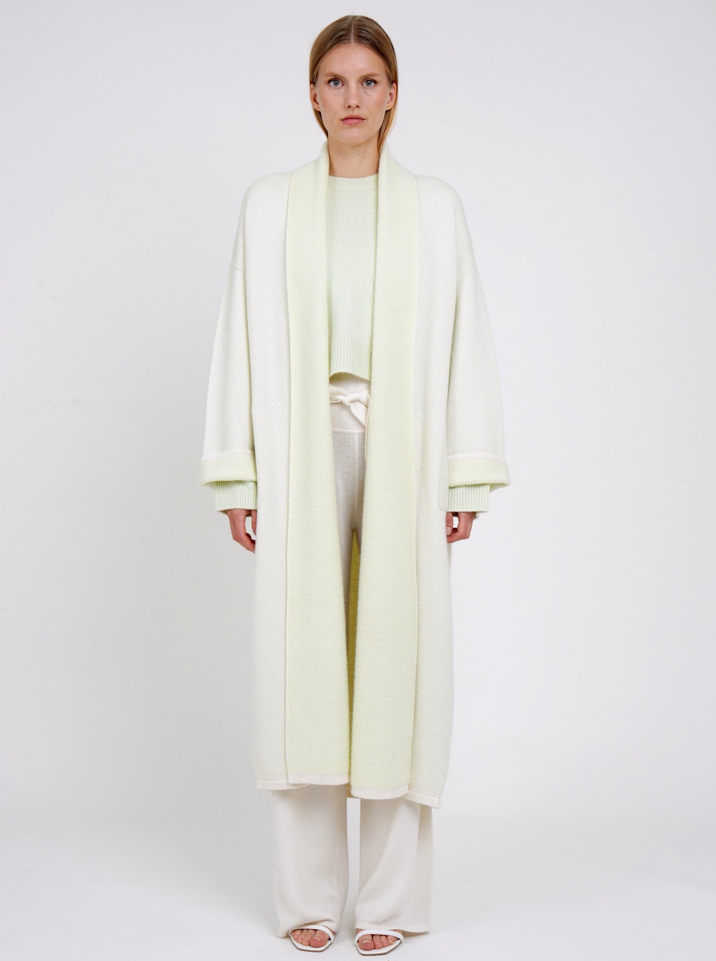 plush knit cashmere curved shape long coat in pale green with shawl collar, wide sleeves over pale green cropped jumper and white knit pants.