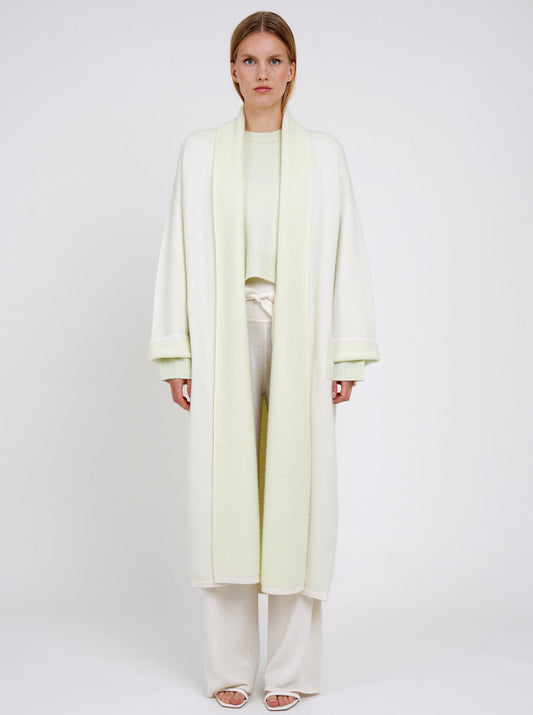 plush knit cashmere curved shape long coat in pale green with shawl collar, wide sleeves over pale green cropped jumper and white knit pants.
