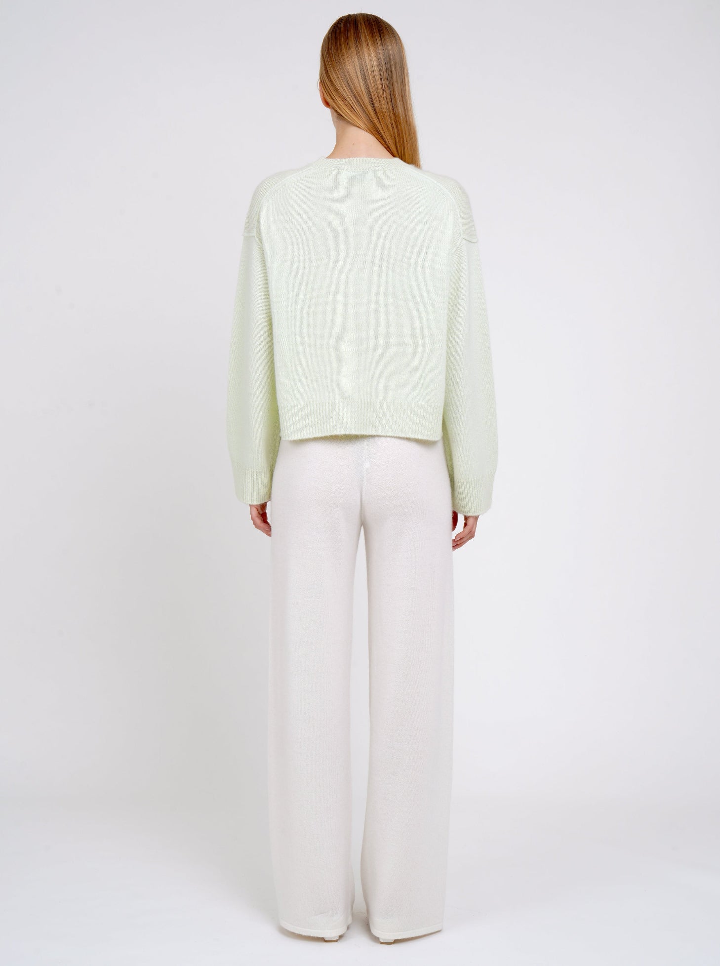 Back view model in light green short jumper with round neck, long sleeves and white cashmere wide leg pants.