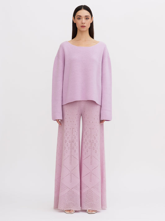 Model wearing a purple-pink cashmere sweater with scoop neck, tie-back, paired with wide-leg, lace knit cashmere trousers.