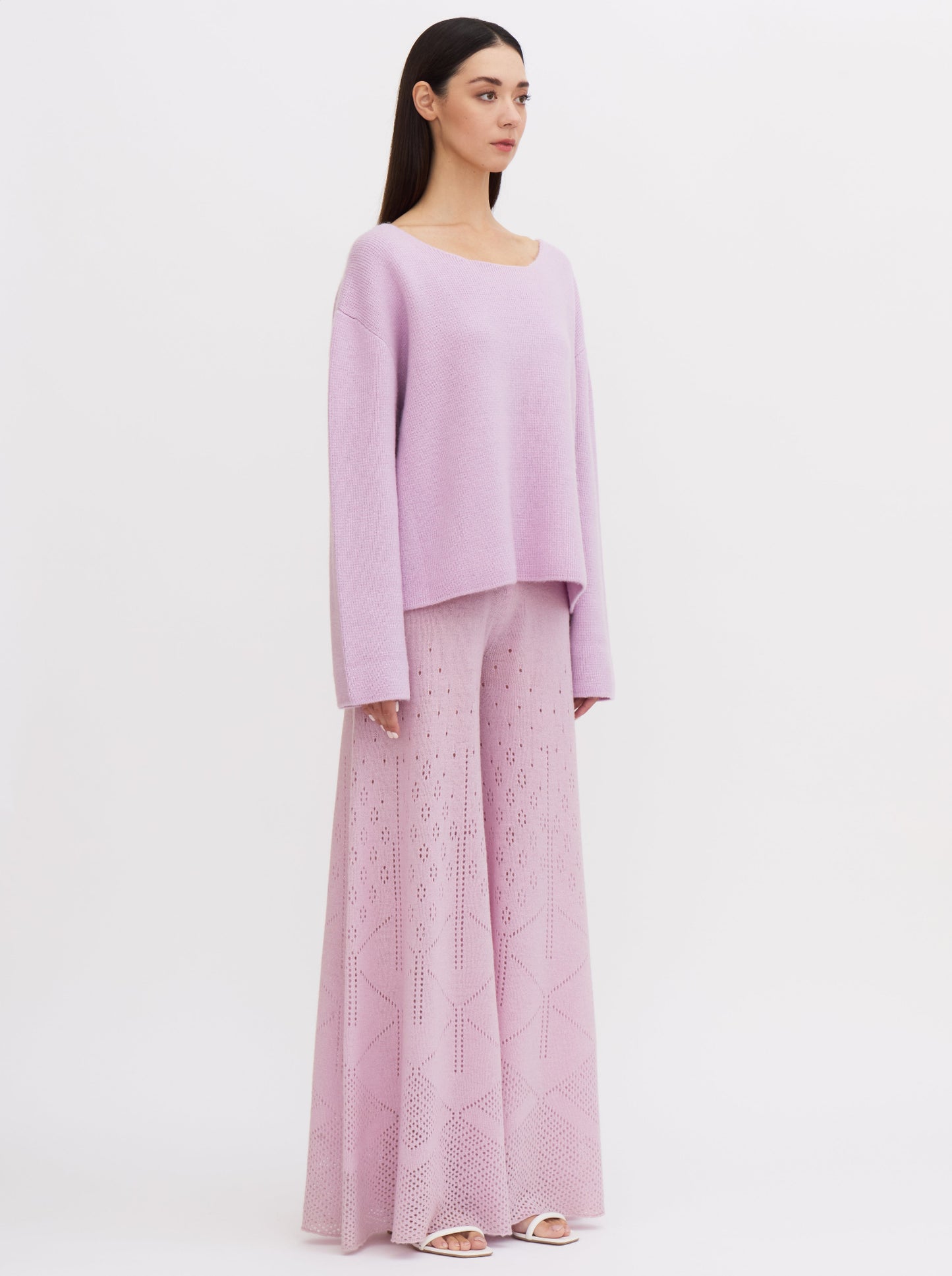 Model wearing a purple-pink cashmere sweater with a tie-back design, paired with wide-leg, lace knit cashmere trousers.