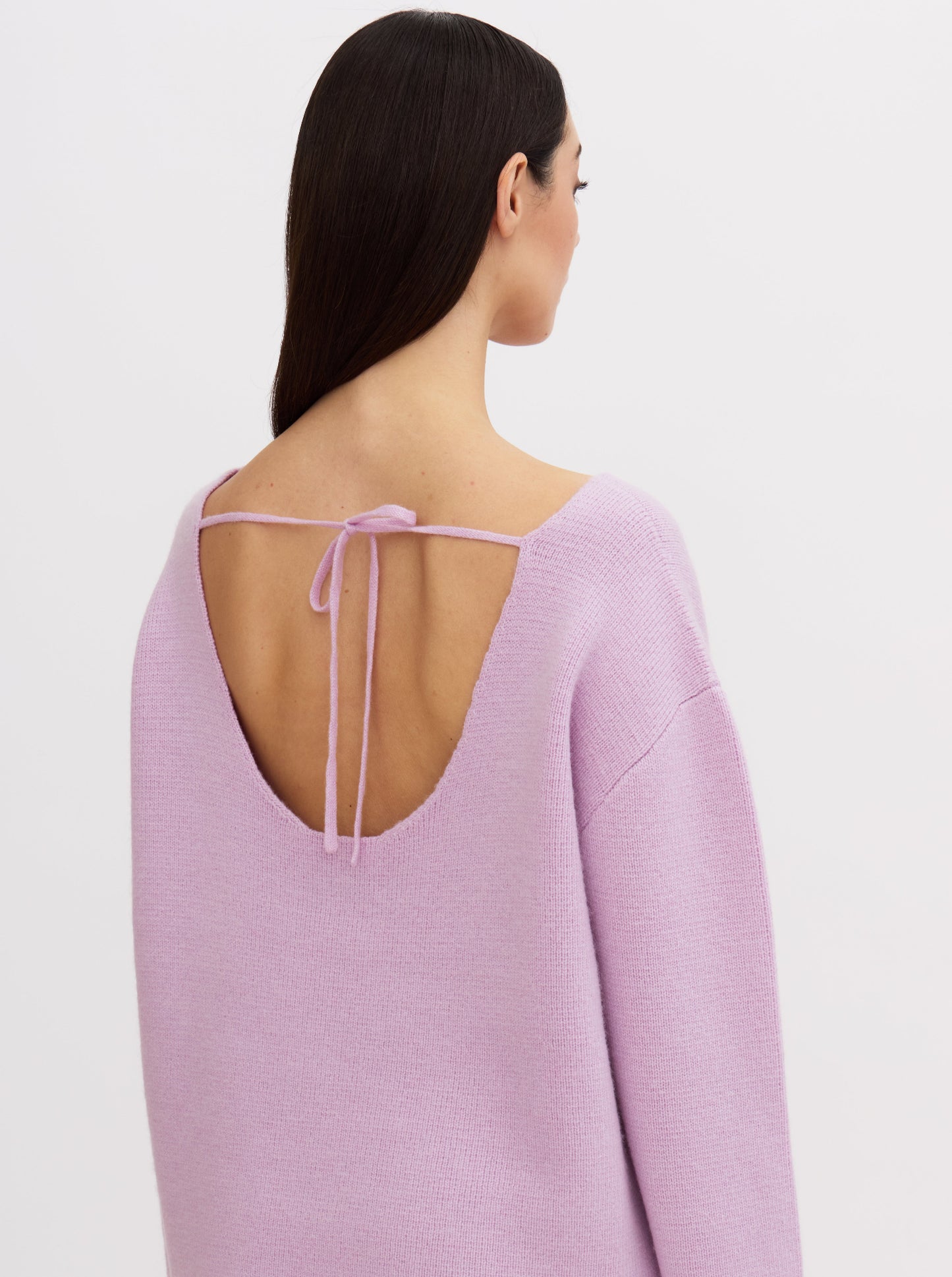 Model wearing a purple-pink cashmere sweater with a tie-back design.