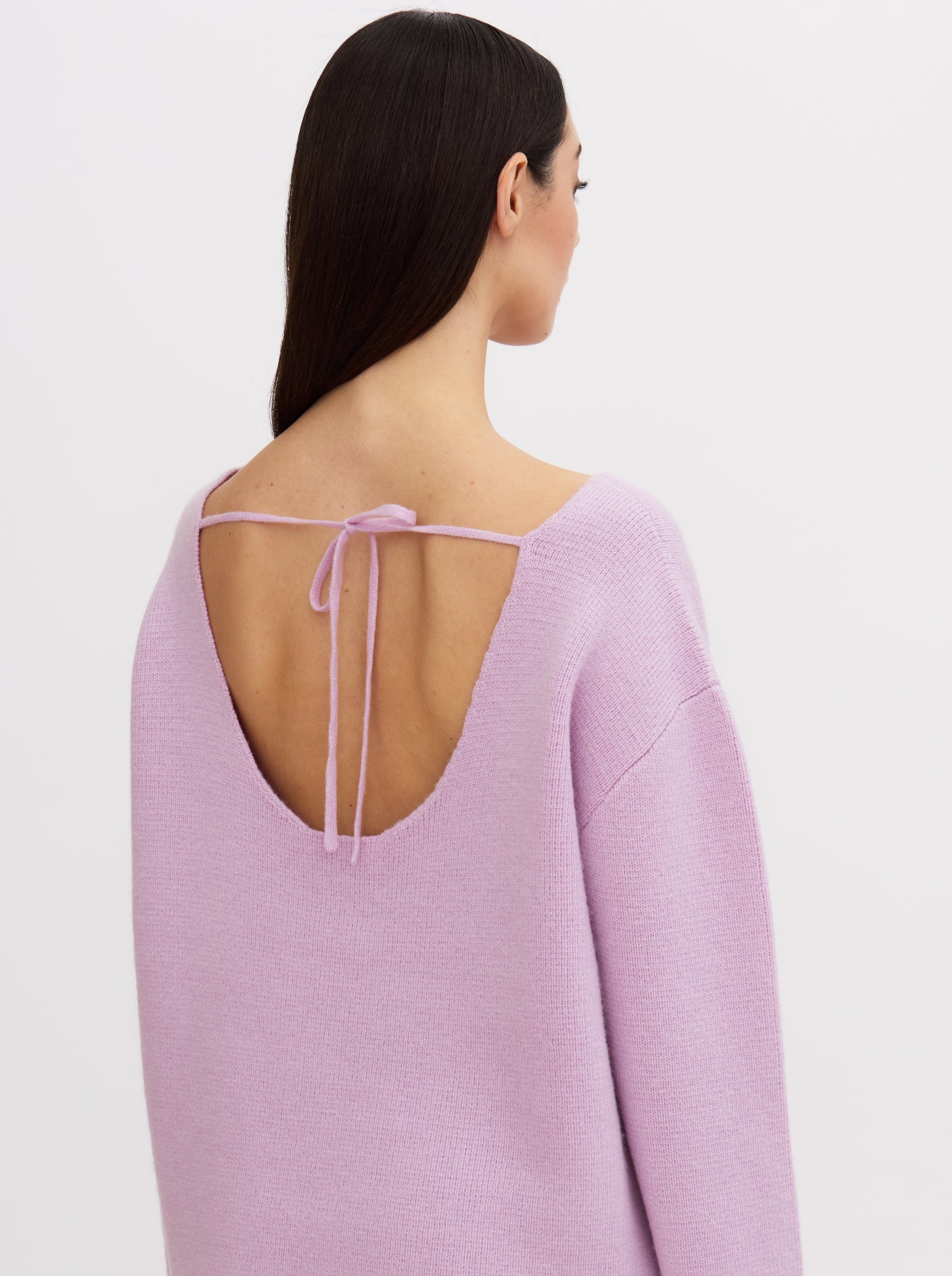 Model wearing a purple-pink cashmere sweater with a tie-back design.
