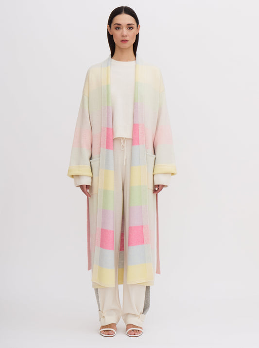 Front view model wears knitted cashmere robe coat in pastel colour rainbow stripes, over white cashmere top and pants.