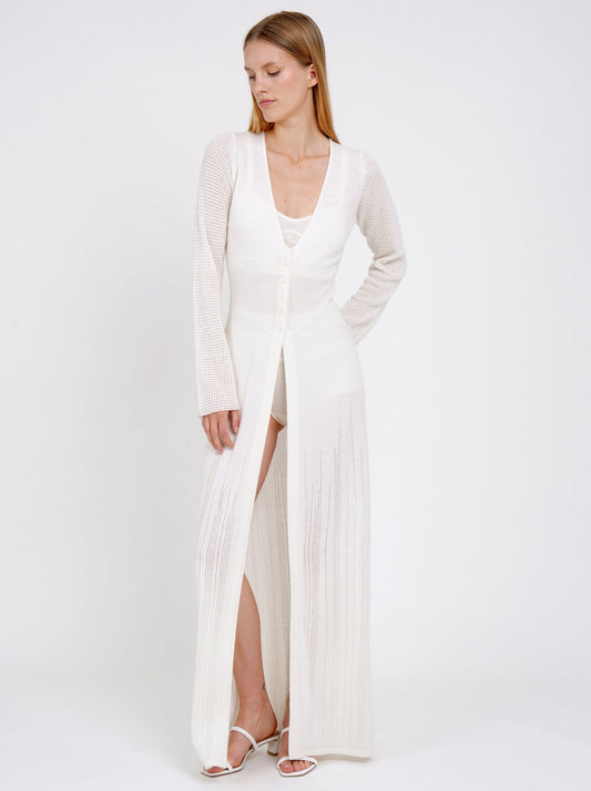 model wears maxi-length long fitted light knit cashmere white cardigan with V neck, long sleeves, buttons through the waist.