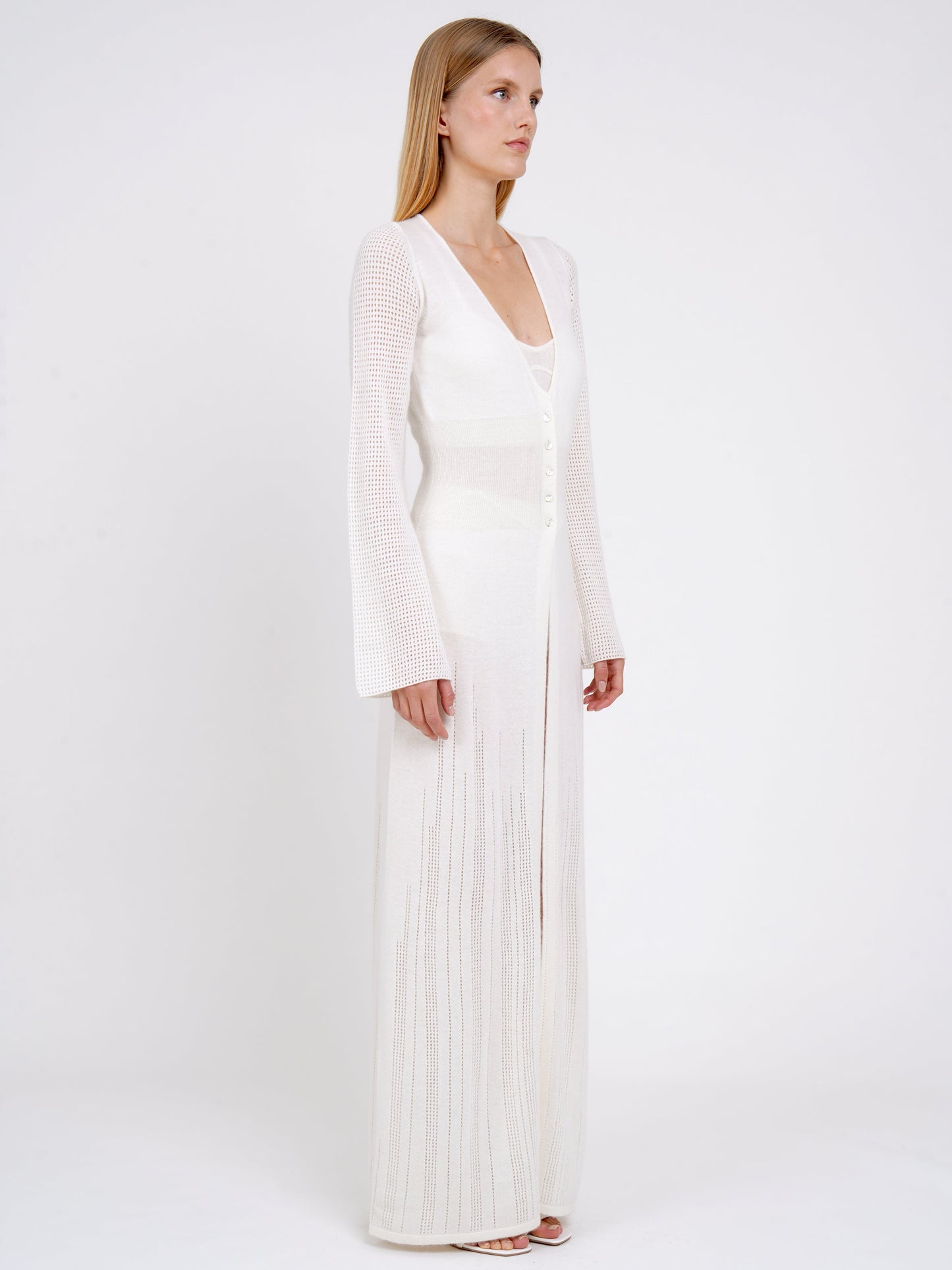 side view model in maxi-length long fitted light knit cashmere white cardigan with deep V neck, long sleeves, buttons through the waist. 