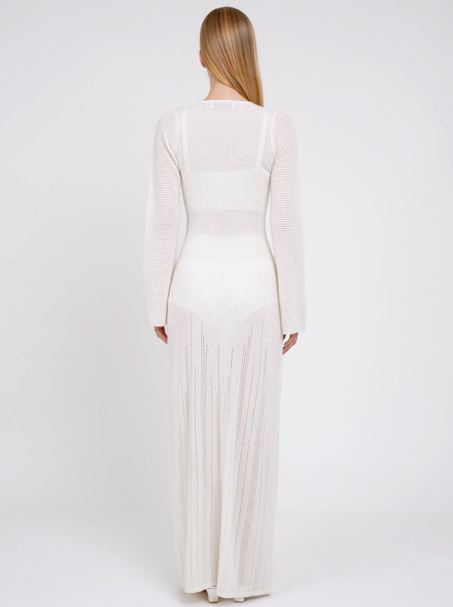 Back view model in maxi-length long fitted light knit cashmere white cardigan with deep V neck, long sleeves, buttons through the waist. 
