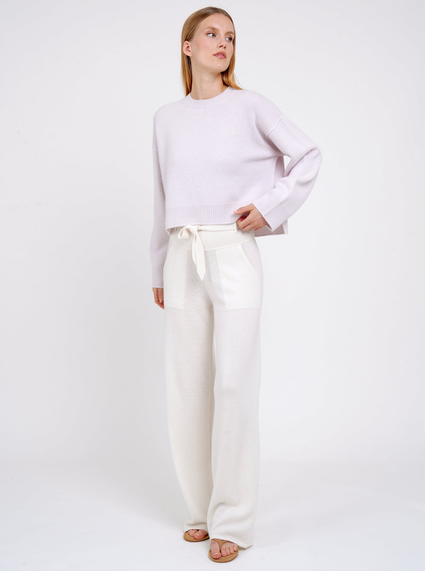 Model wears pure white cashmere, wide leg pants with matching belt and lilac cashmere round neck jumper. 