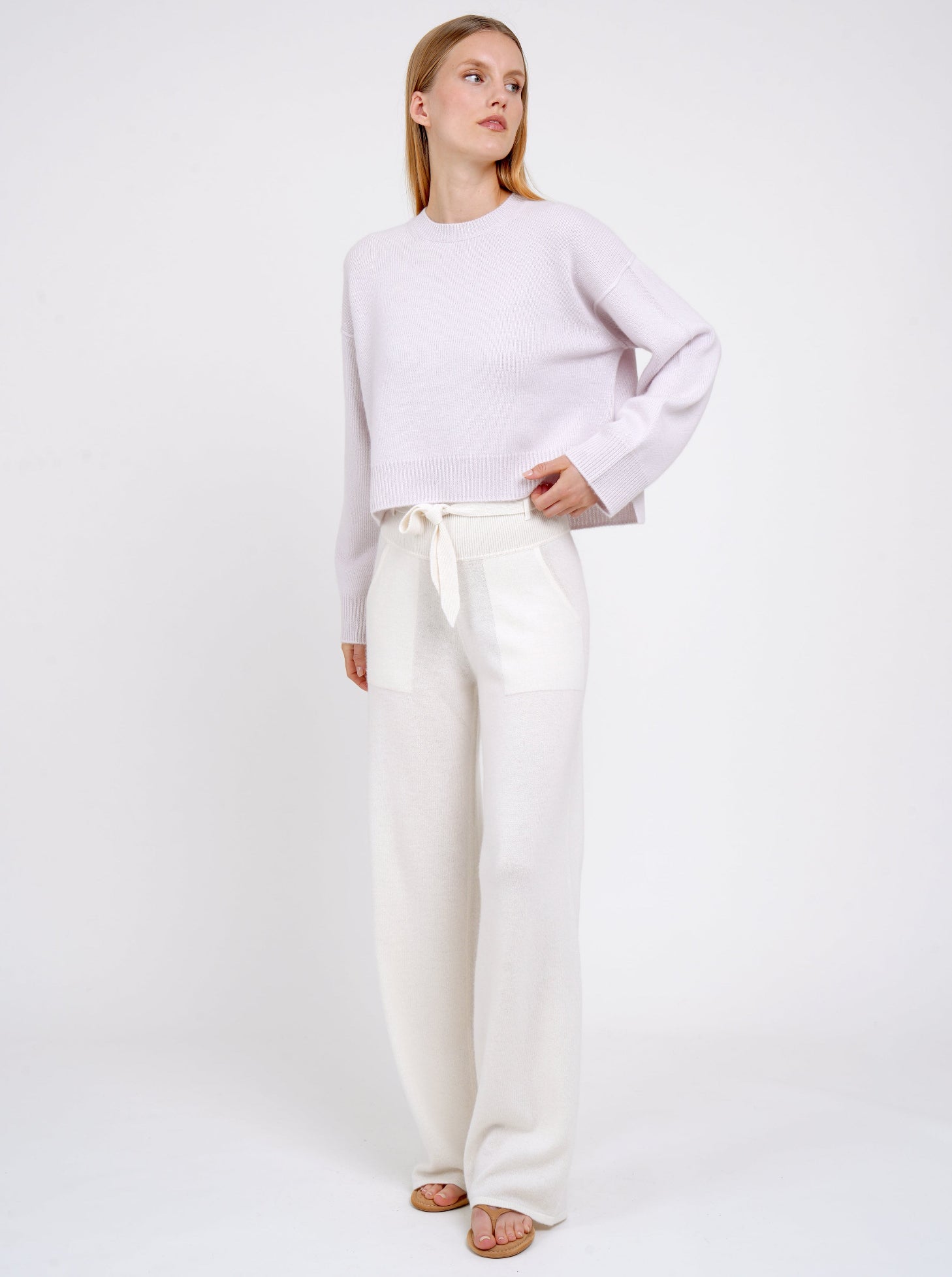 Model wears pure white cashmere, wide leg pants with matching belt and lilac cashmere round neck jumper. 