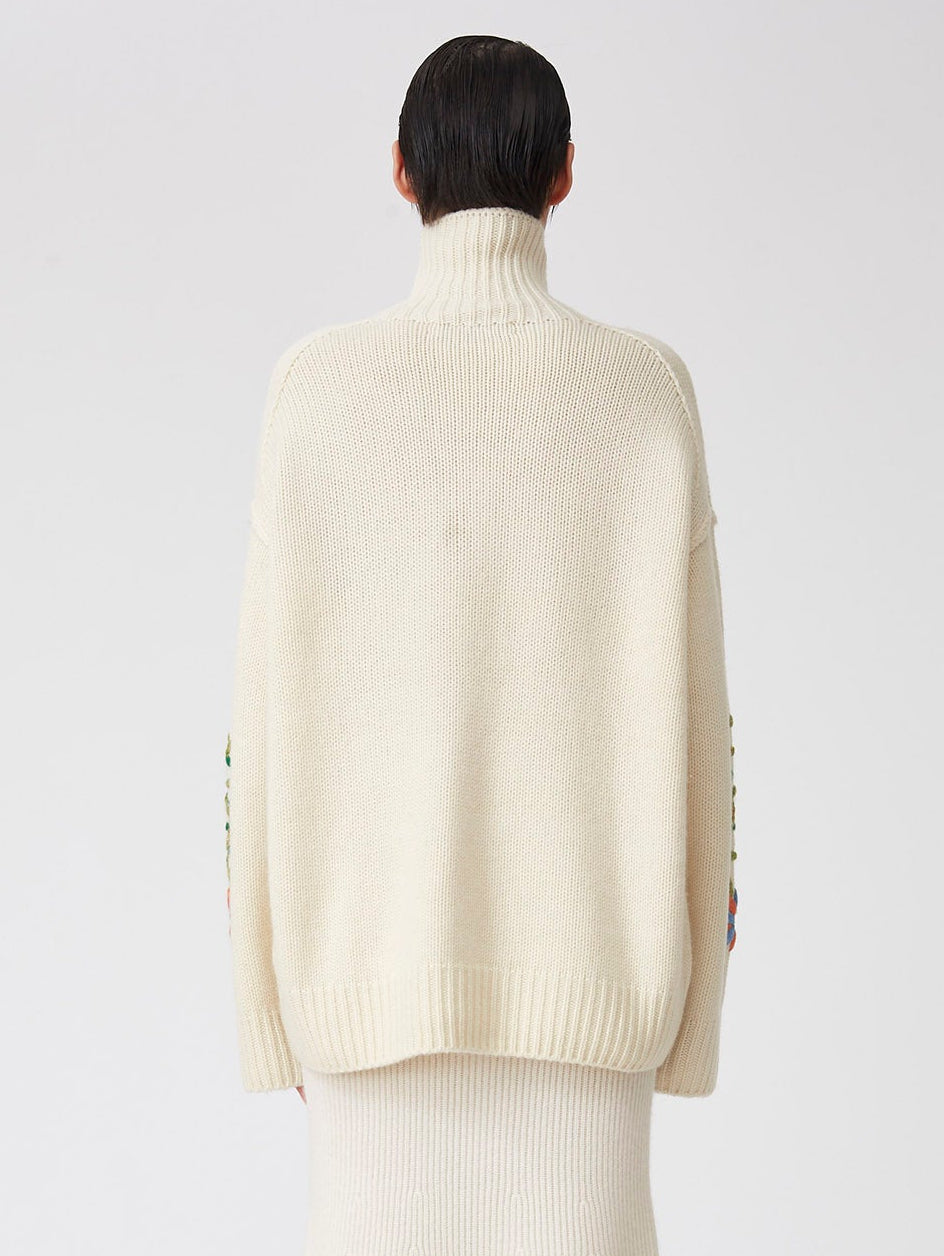 Cropped back view of model wearing oversized chunky knit white roll neck sweater; worn over white knit midi skirt.