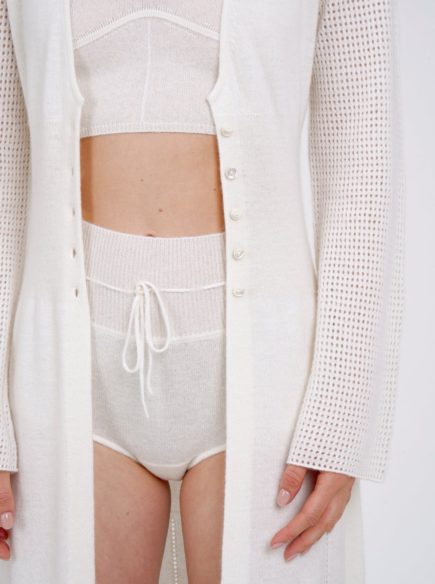 Cropped close-up showing cashmere knit detail of wears long white knit cardigan over white cashmere shorts with drawstring waist and white knit cropped bra top.