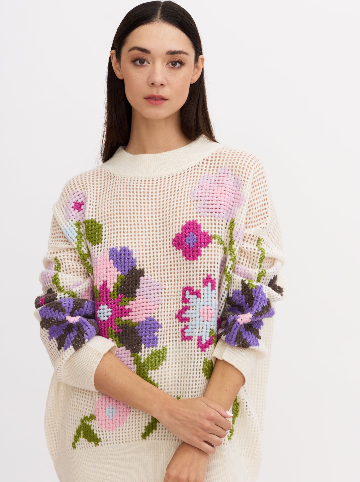 Cropped image of model wearing white net-knit cashmere round neck sweater showing full detail of hand embroidered cross-stitch floral pattern in multi-coloured cashmere yarns.