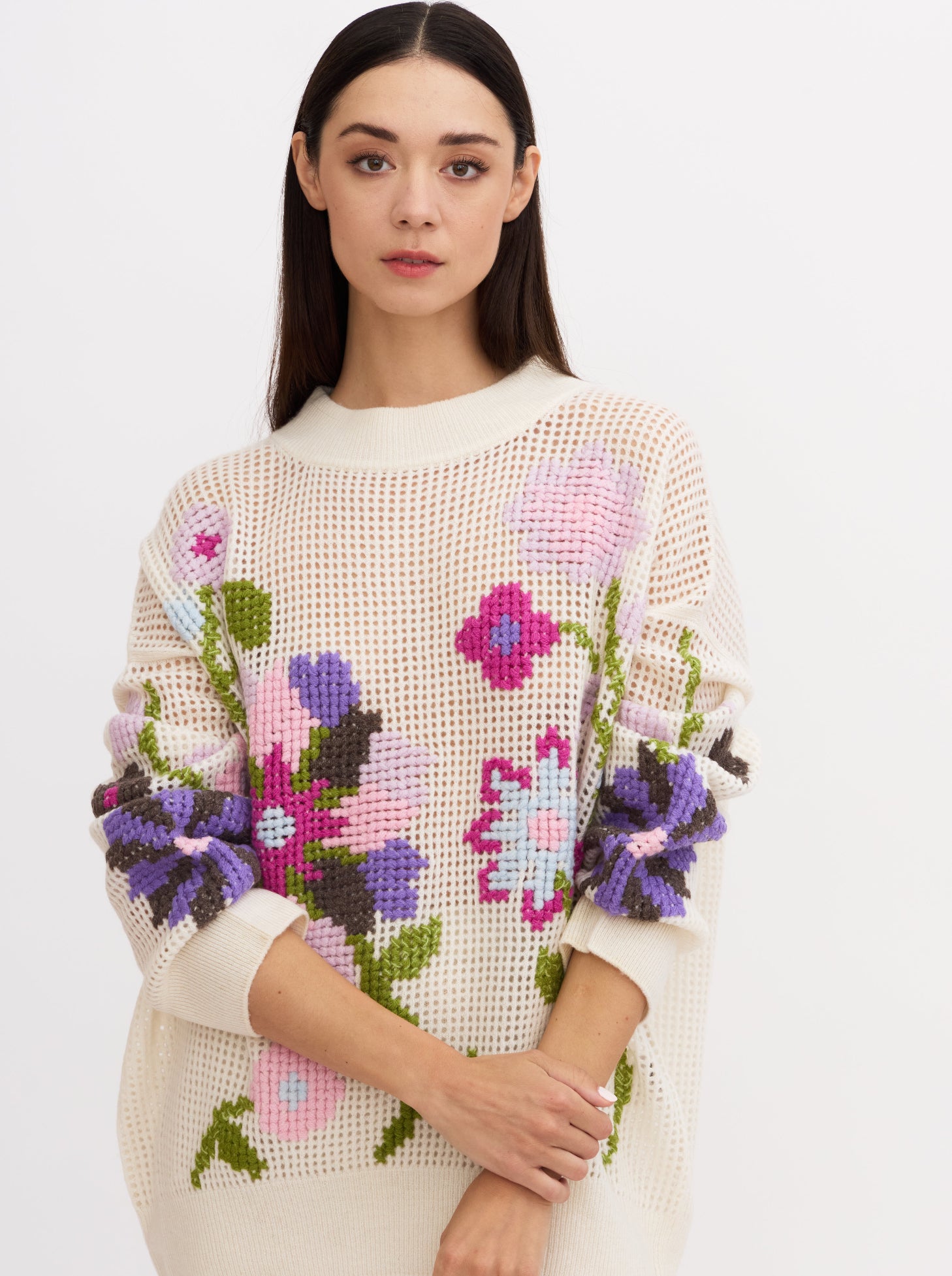 Cropped image of model wearing white net-knit cashmere round neck sweater showing full detail of hand embroidered cross-stitch floral pattern in multi-coloured cashmere yarns.