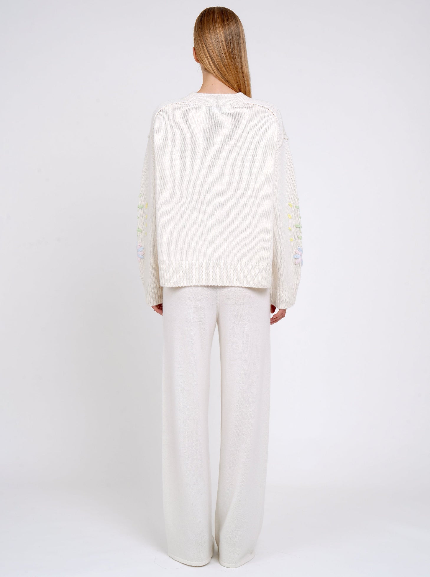 Back view model wearing a white cashmere cardigan worn with white cashmere wide-leg pants.