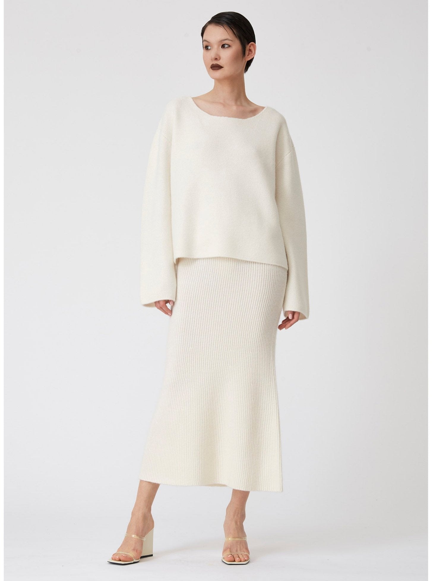 Modal wears low calf length white ribbed knit flared skirt with baggy white cashmere long sleeve jumper.