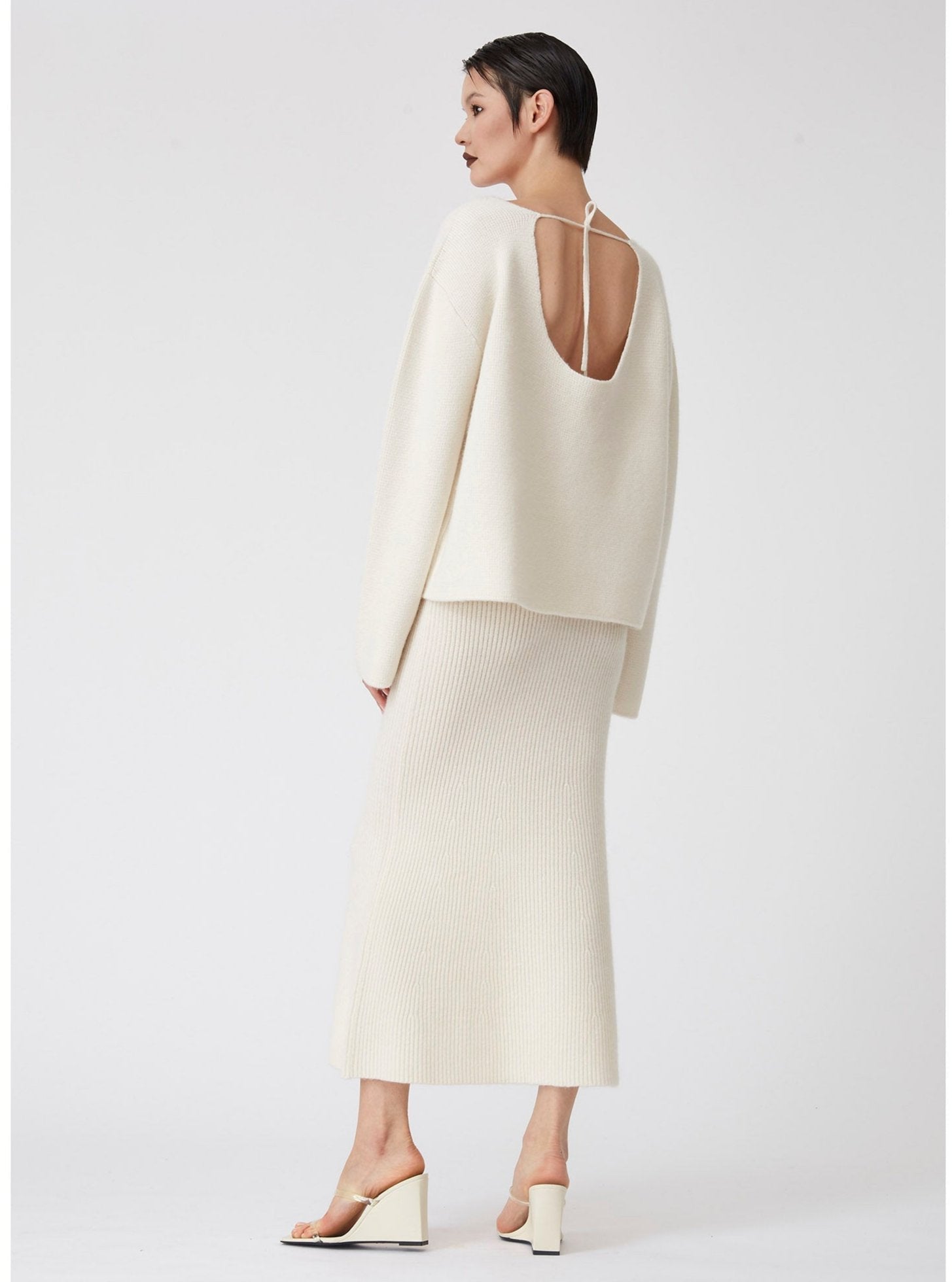 Side back view model with white cashmere ribbed knit midi skirt with long sleeve, low back white cashmere jumper.