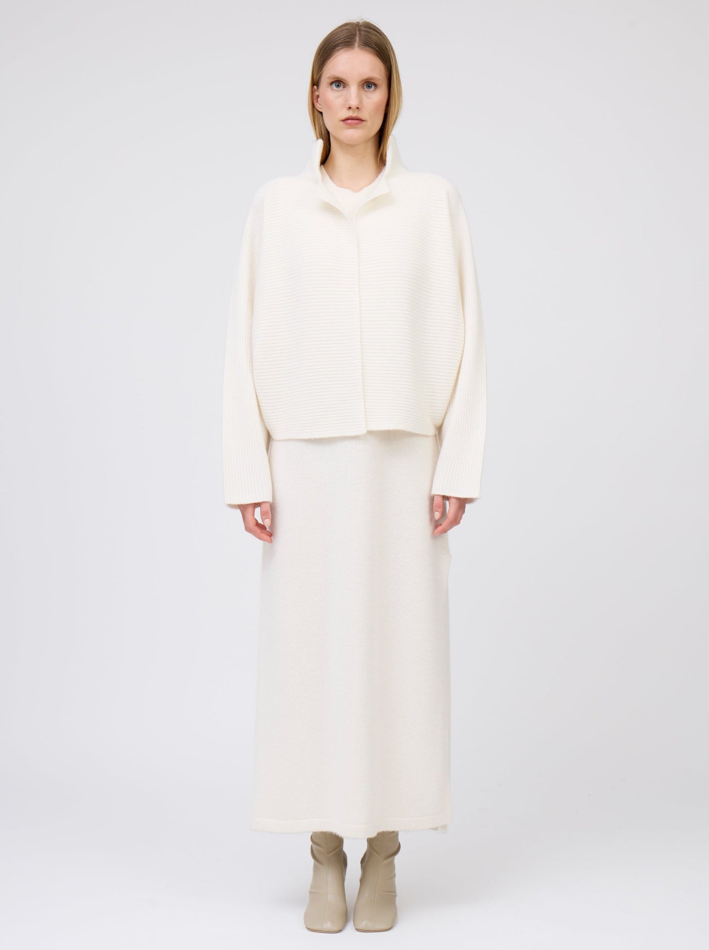 Front view model in relaxed fit white ribbed knit cashmere short jacket with high collar and kimono sleeves, worn with long straight white cashmere knit dress. 