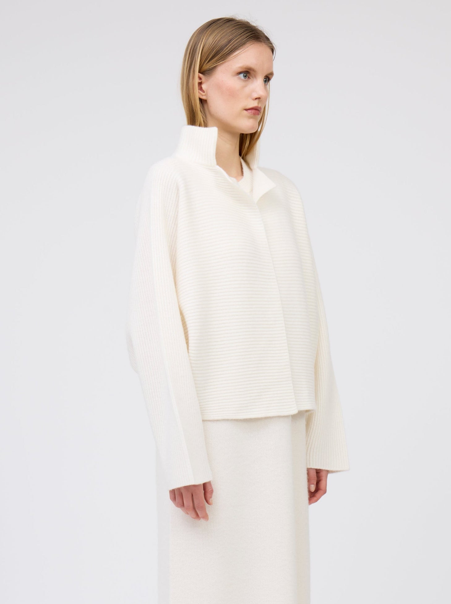 close-up side view model in white ribbed knit cashmere short jacket with collar and kimono sleeves, with long straight white cashmere knit dress underneath.