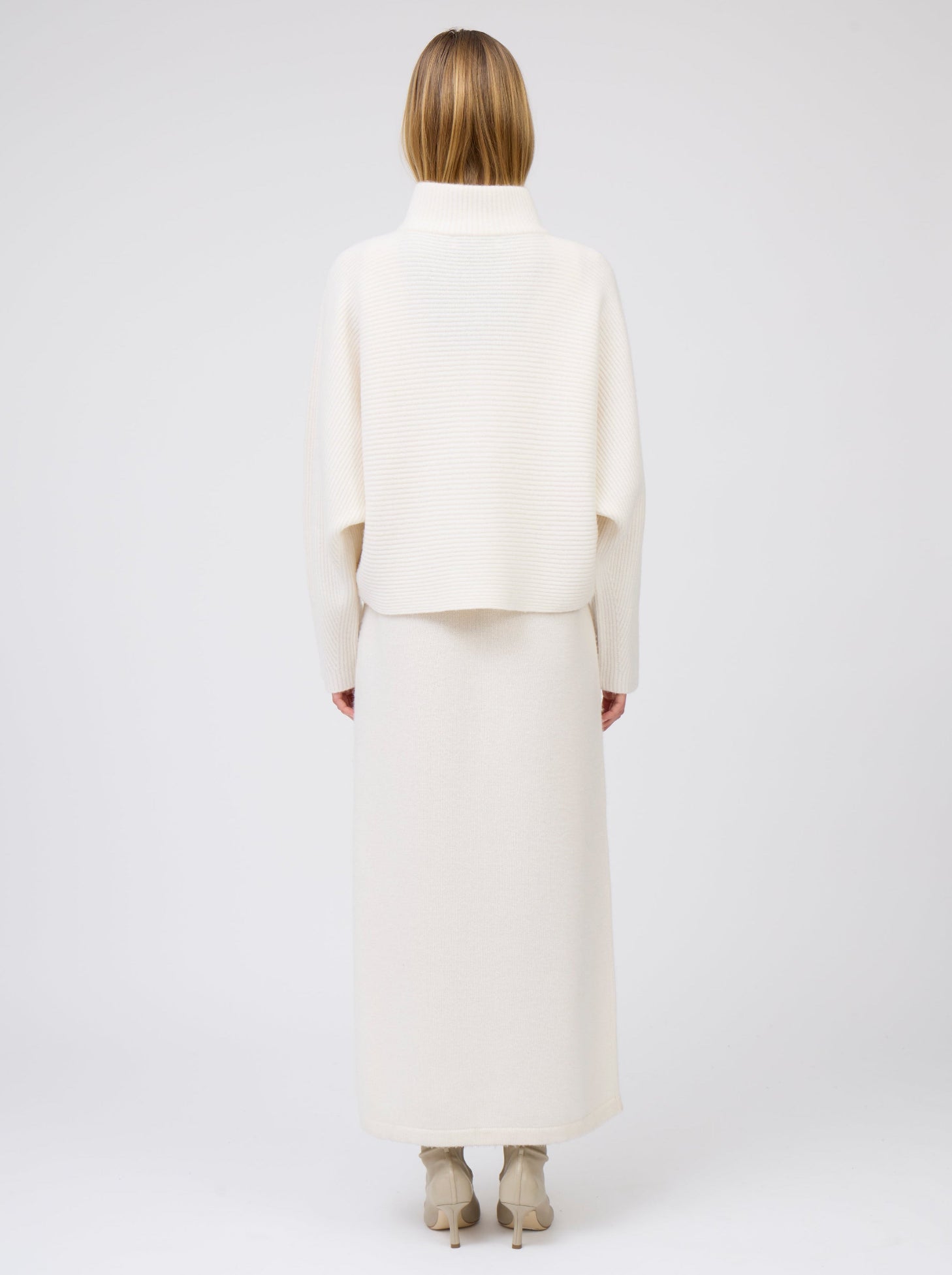 Back view model in white ribbed knit cashmere short jacket with collar and kimono sleeves, worn with long white cashmere knit dress.