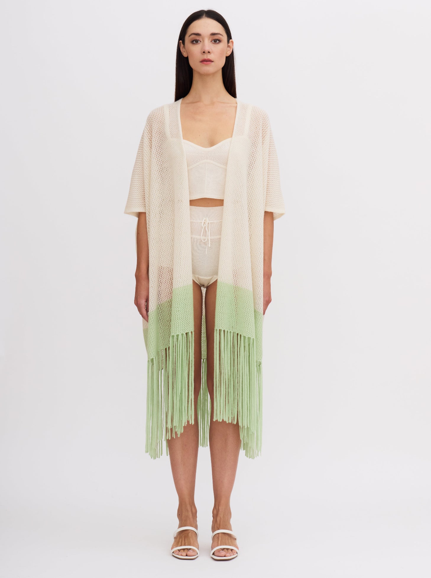 Front view of model wearing light weight cashmere knit cover up in white with mint green fringed hem, over cashmere knit bodice top and bottoms.