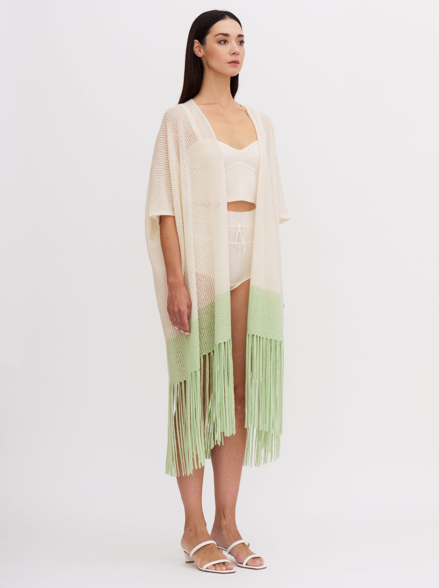 Model wears light weight cashmere knit cover up in white with elbow length sleeves and mint green fringed hem, over white cashmere knit bodice top and bottoms.