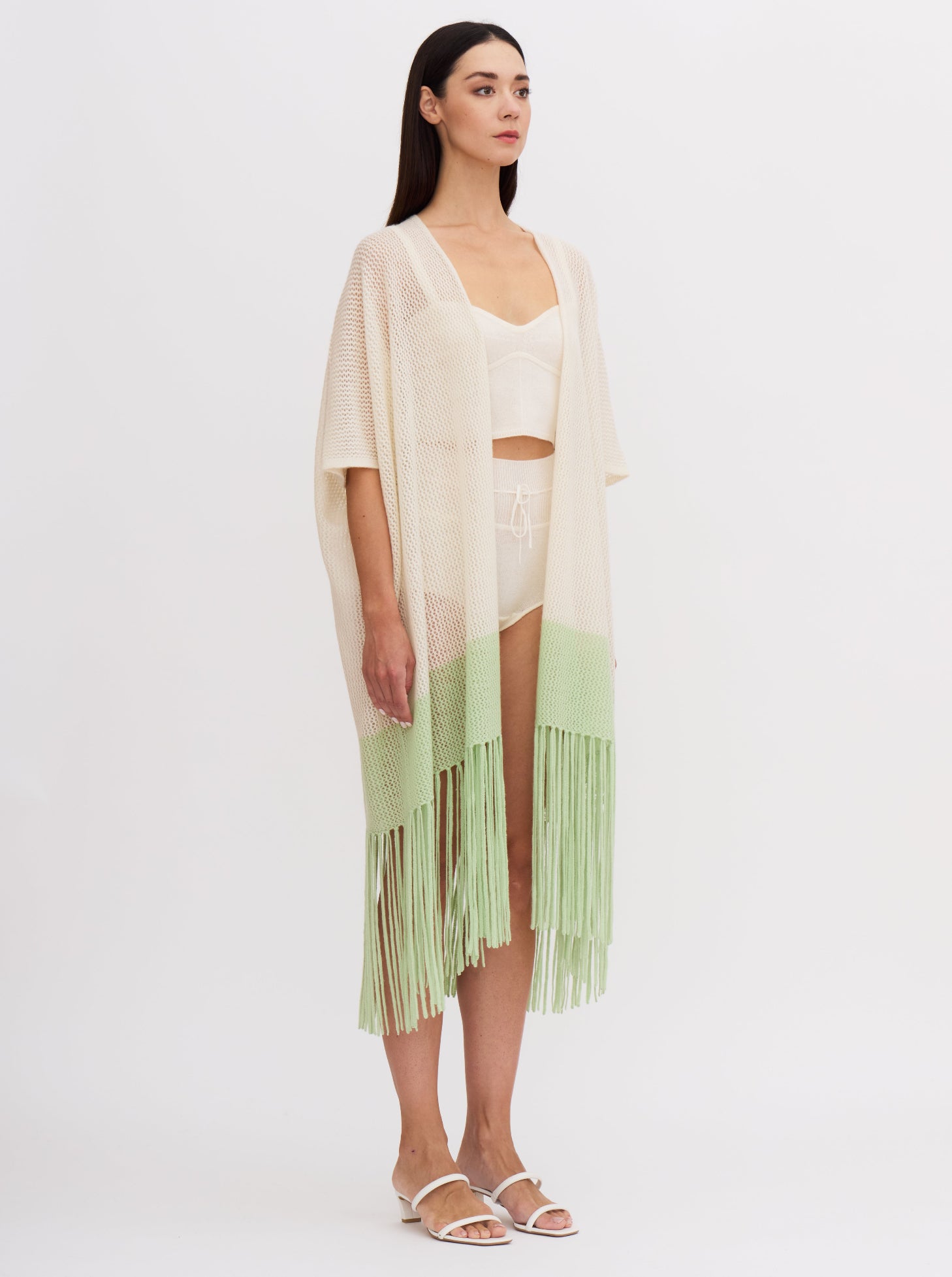 Model wears light weight cashmere knit cover up in white with elbow length sleeves and mint green fringed hem, over white cashmere knit bodice top and bottoms.