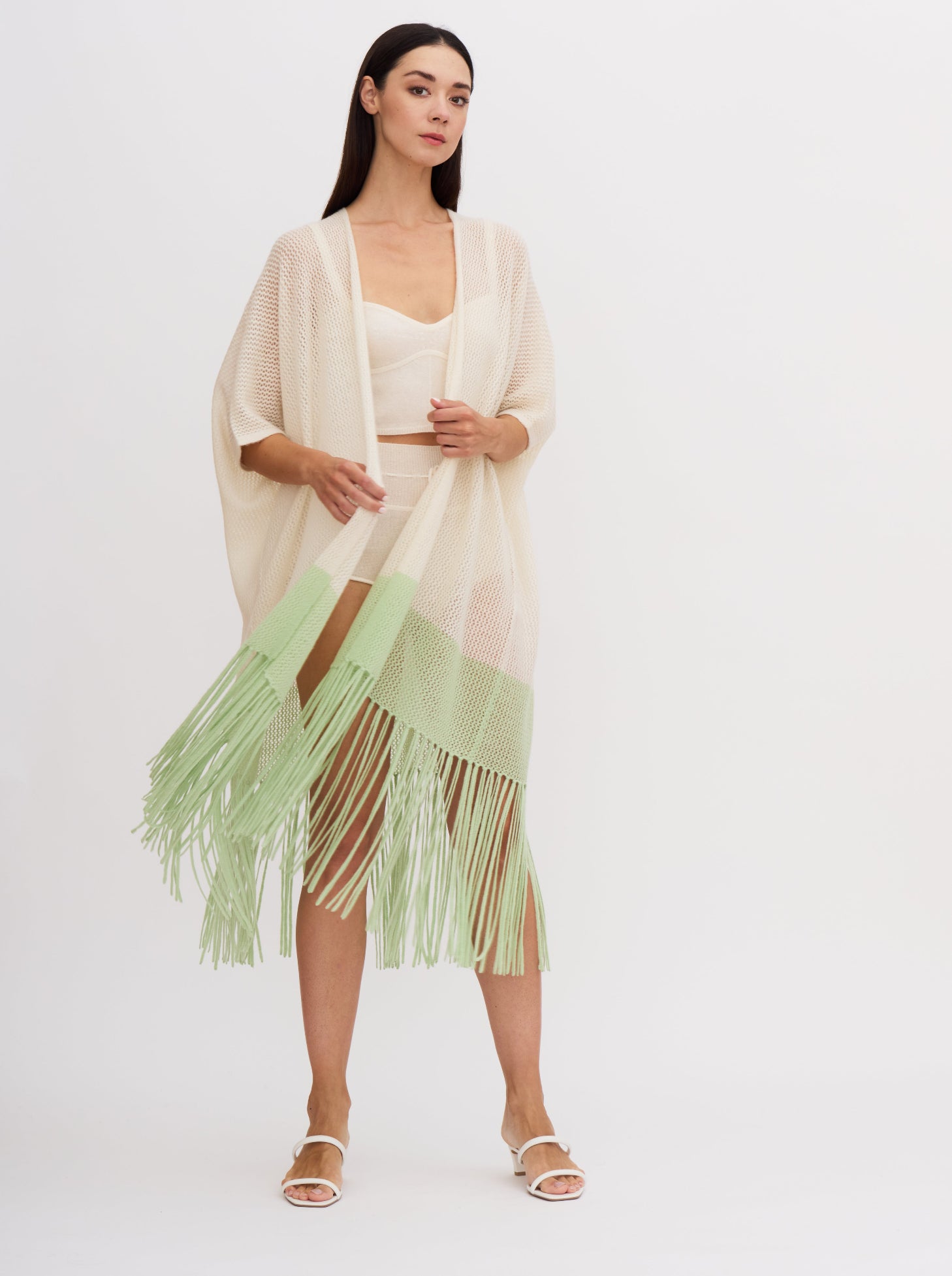 Model wears light weight cashmere knit cover up in white with mint green, over white cashmere knit bodice top and bottoms, showing the fringed hem in flowing movement.