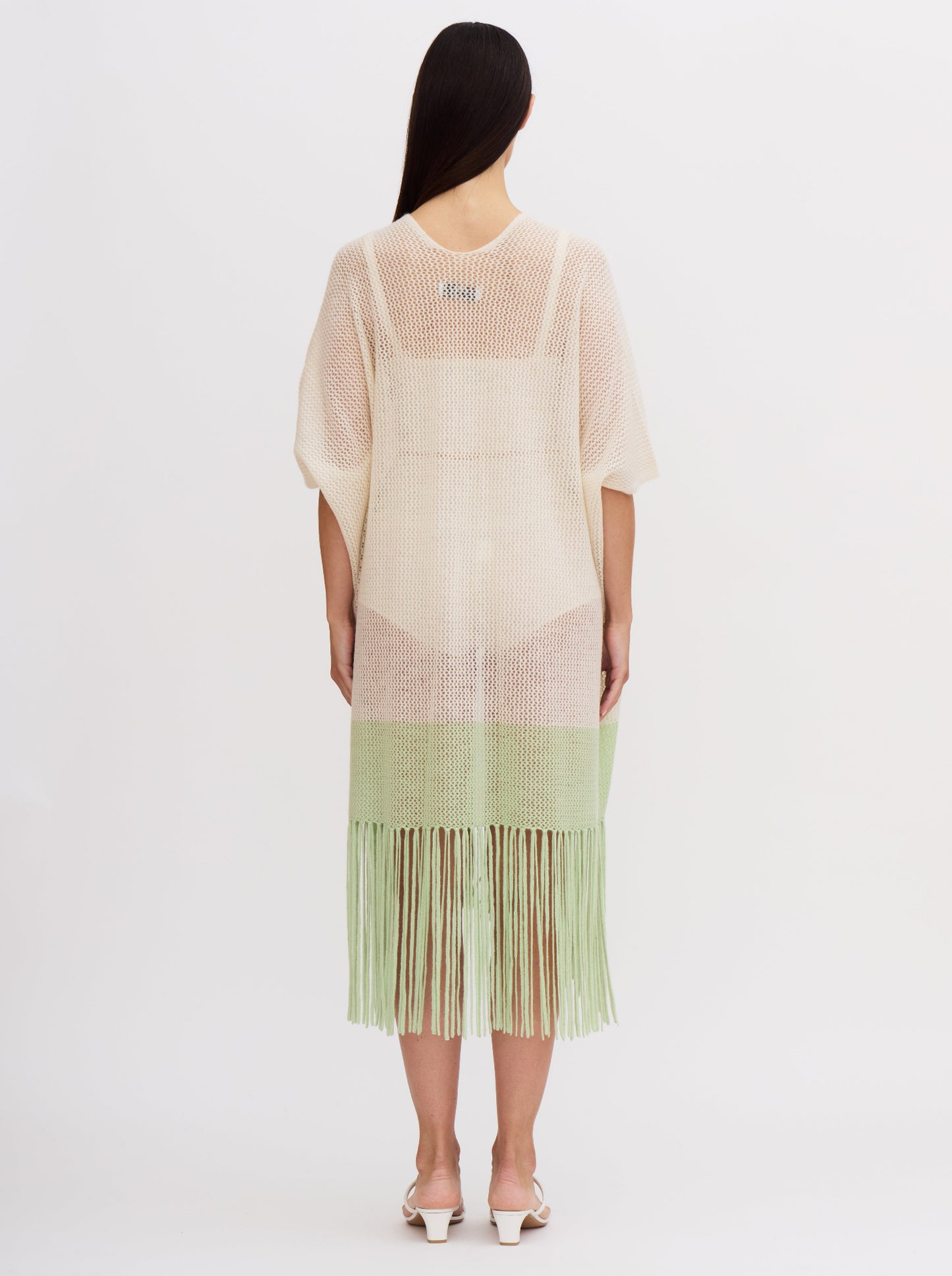 Back view of model wearing light weight cashmere knit cover up in white with mint green fringed hem.