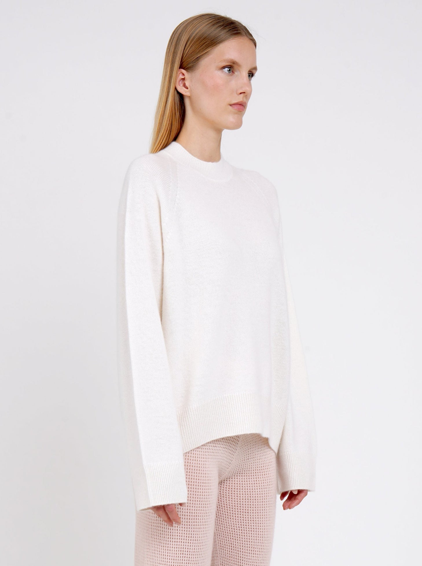 Close up model in white cashmere jumper with round neck and long sleeves and pale peach pink knit cashmere pants.