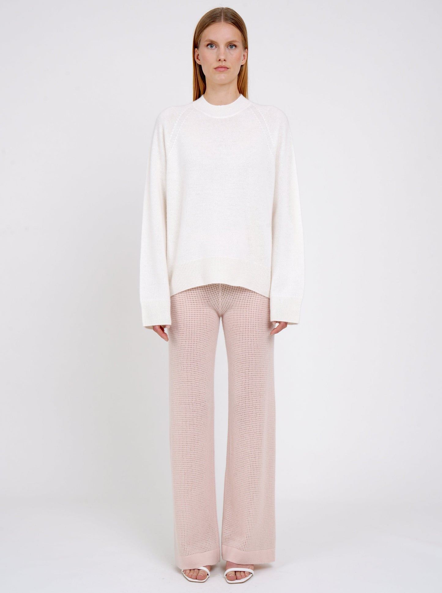 Front view model in white cashmere jumper with round neck, long sleeves and pale peach pink knit cashmere pants.