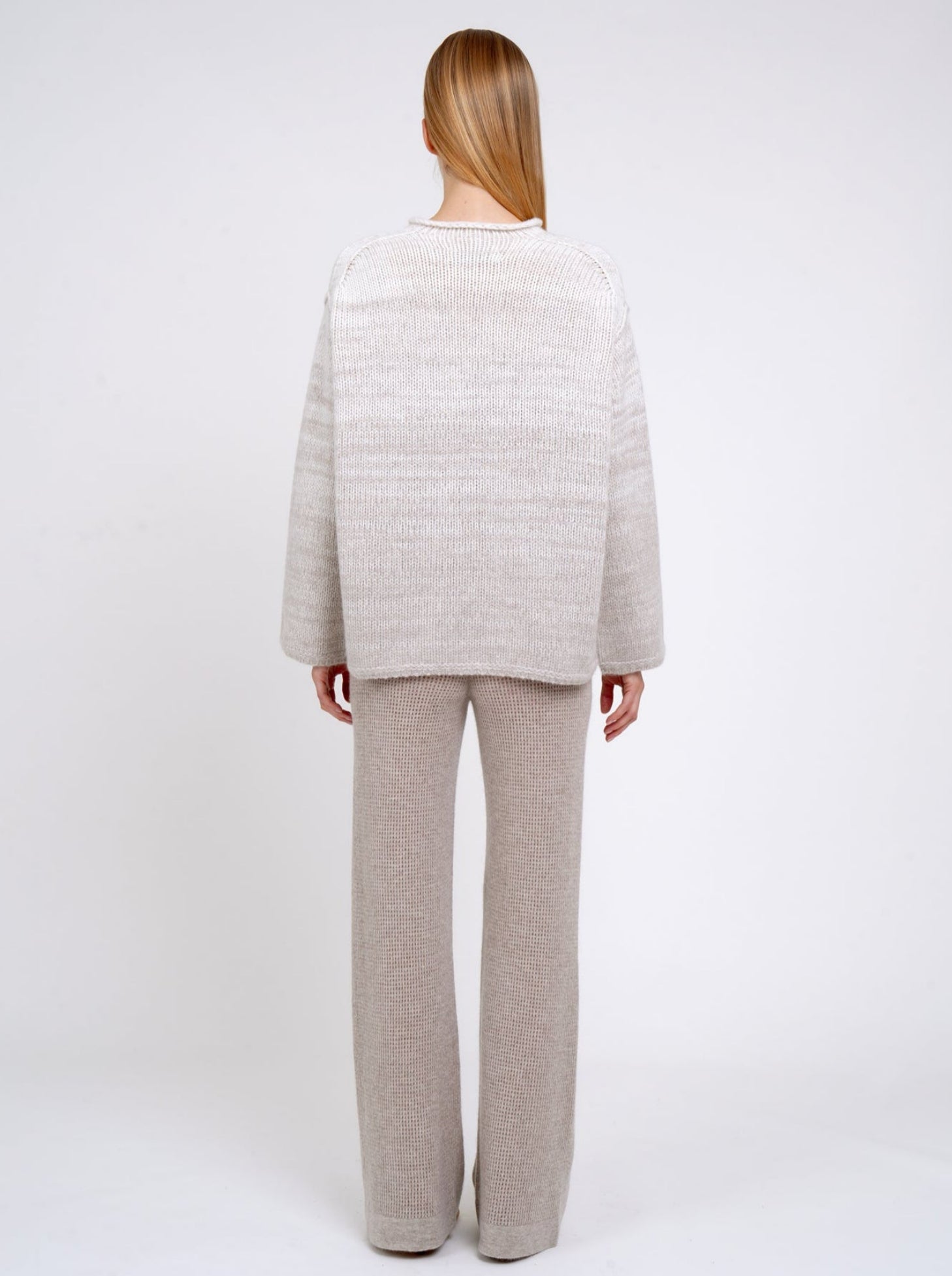 Back view of model in relaxed fit mixed colour knitted jumper in natural white and beige, with round neck; worn with new beige cashmere knit pants.