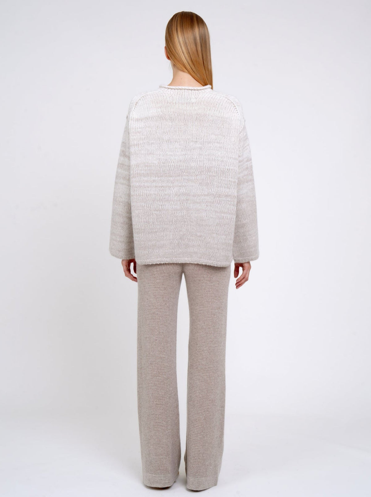 Back view of model in relaxed fit mixed colour knitted sweater in natural white and beige, with round neck; worn with new beige cashmere knit pants.