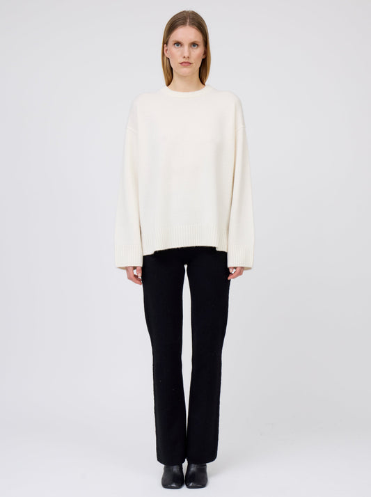Front view of model wearing creamy white oversized round neck sweater with black suit pants and black boots.