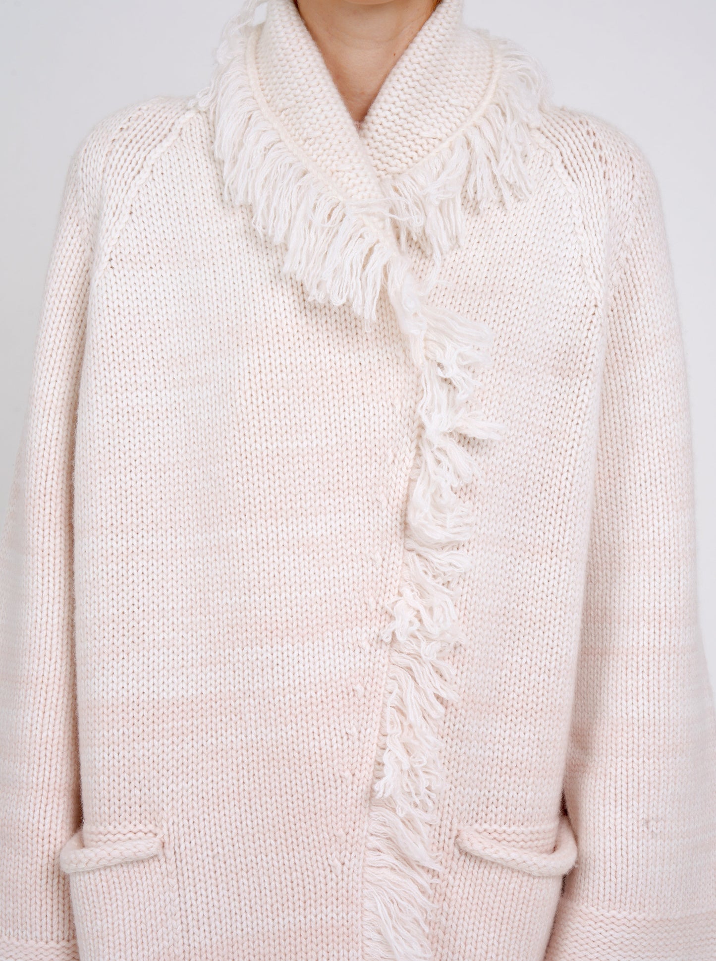 close-up showing chunky knit detail of coat in pale peach cashmere blended with white, with shawl collar, fringe trim, patch pockets.