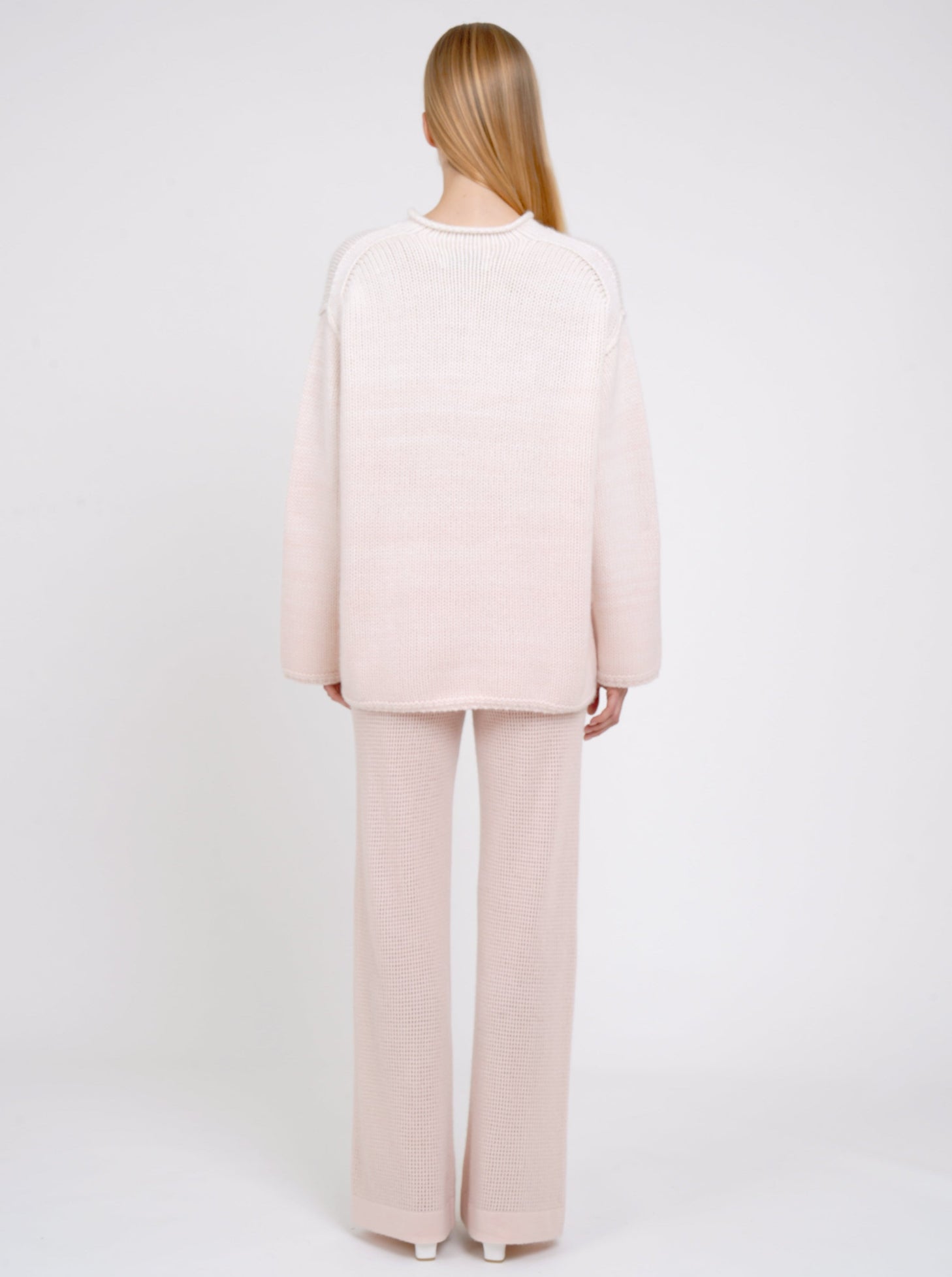 back view of model in relaxed fit mixed colour chunky knit jumper in peach and white with matching peach net knit pants.