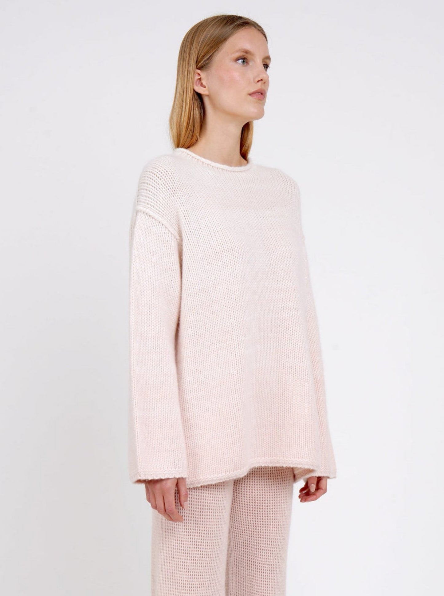 close-up side view of model in relaxed fit mixed colour chunky knit jumper in peach and white with matching peach net knit pants.