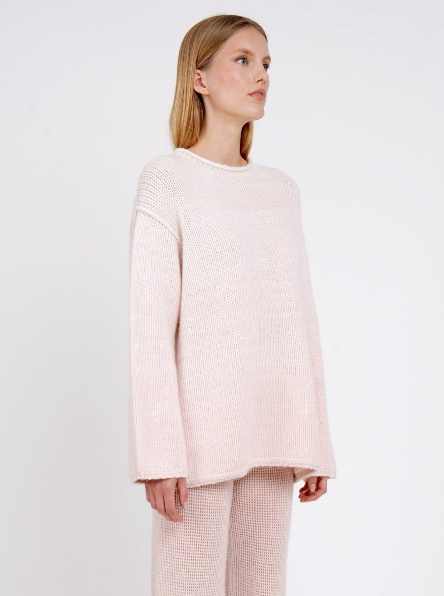 close-up side view of model in relaxed fit mixed colour chunky knit jumper in peach and white with matching peach net knit pants.