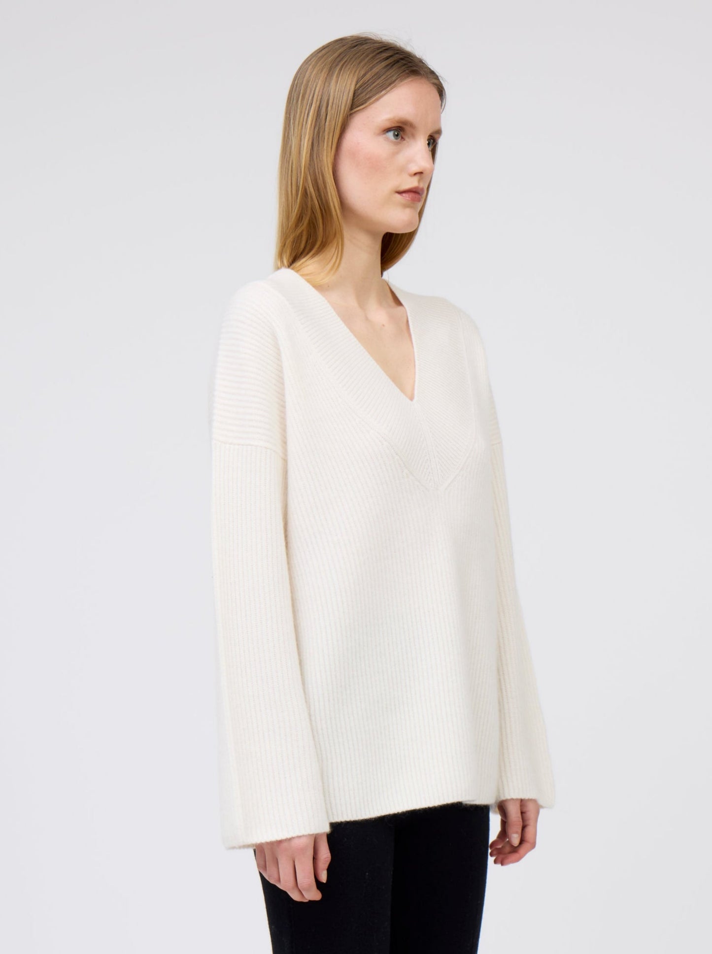 Close-up side view of model wearing creamy white V-neck ribbed knit cashmere sweater with generous long sleeves.