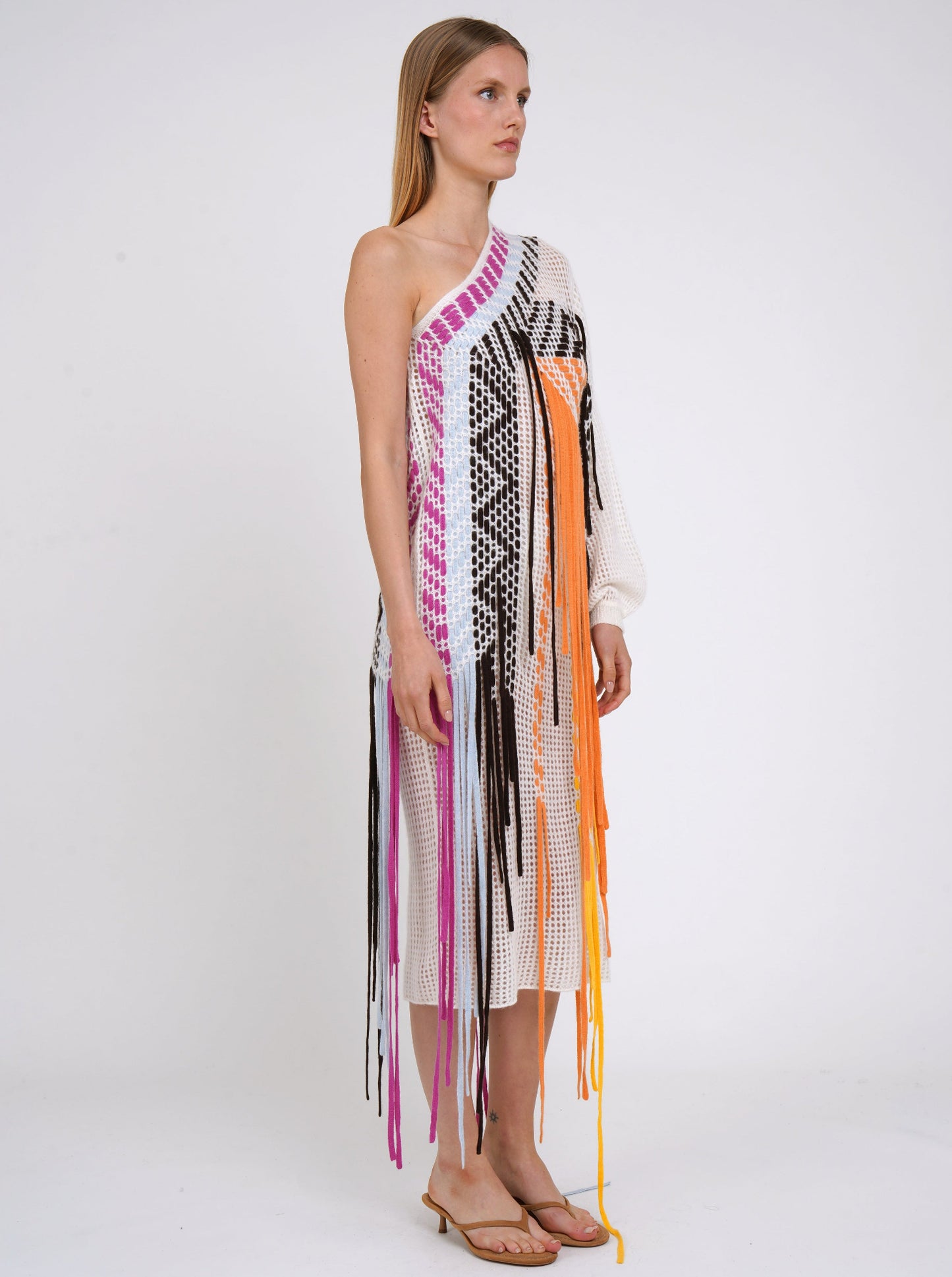side view white light weight cashmere knit one shoulder shift dress with asymmetric neckline, decorated with woven coloured fringes which fall to the ground.