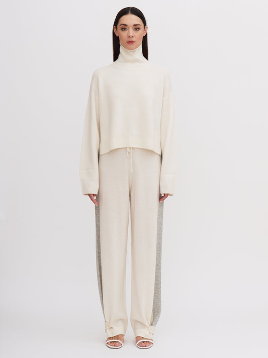 Front view of model wearing white cashmere, cropped length, roll neck jumper with white wide leg pants.