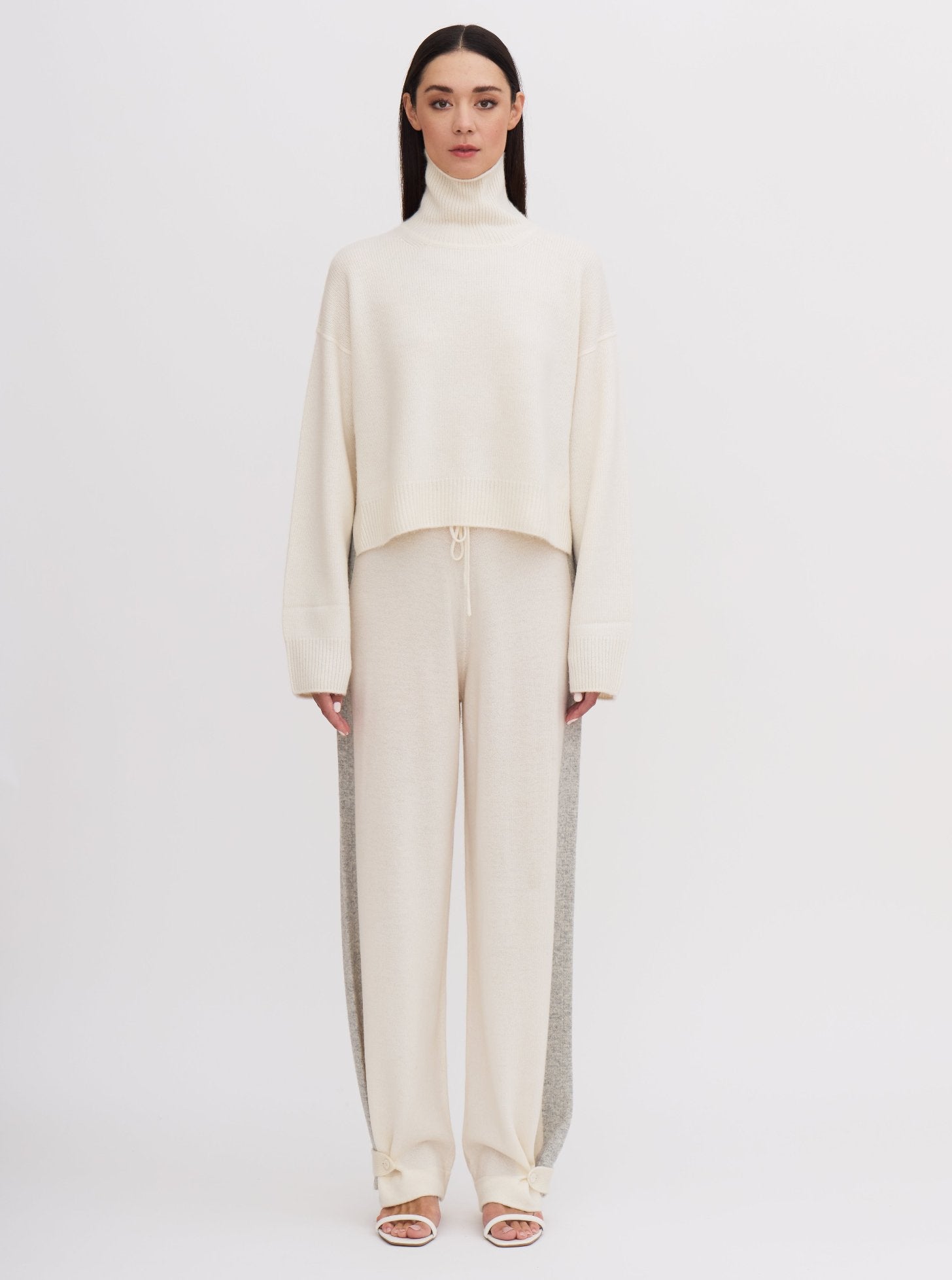 Front view of model wearing white cashmere, cropped length, roll neck sweater with white wide leg pants.