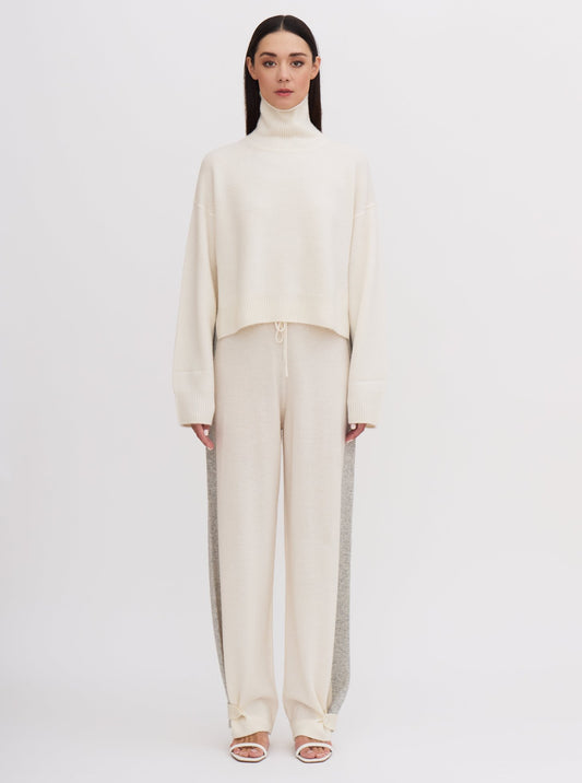 Front view of model wearing white cashmere, cropped length, roll neck sweater with white wide leg pants.