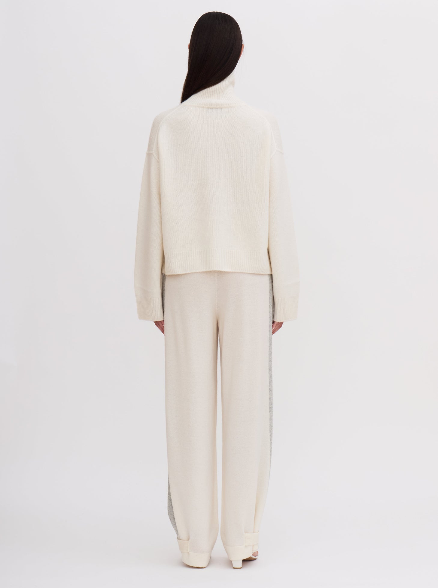 Back view of model wearing white cashmere, cropped, roll neck sweater with white wide leg pants.