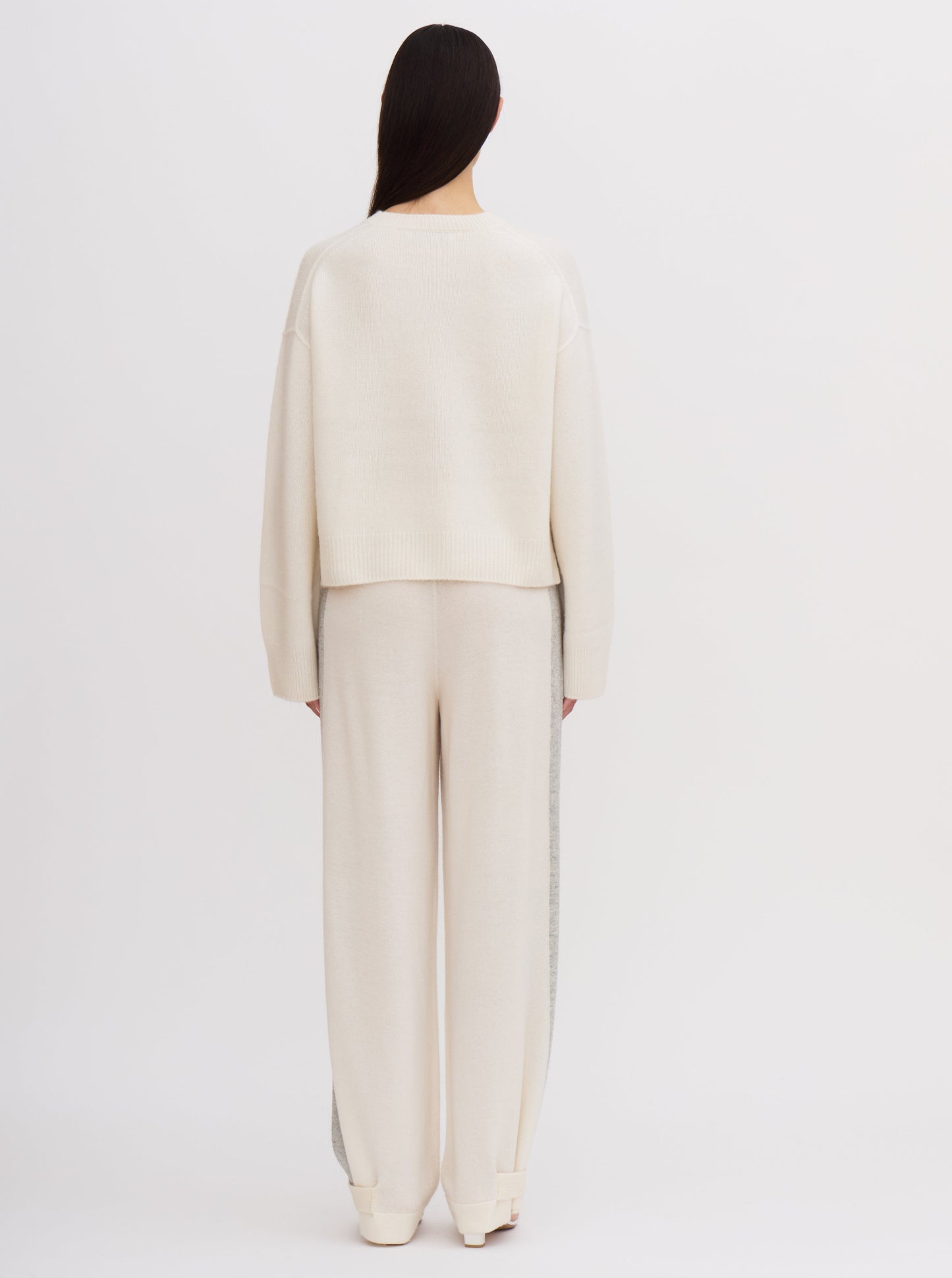 Back view of model wearing white cropped length round neck cashmere sweater and white wide leg cashmere pants.