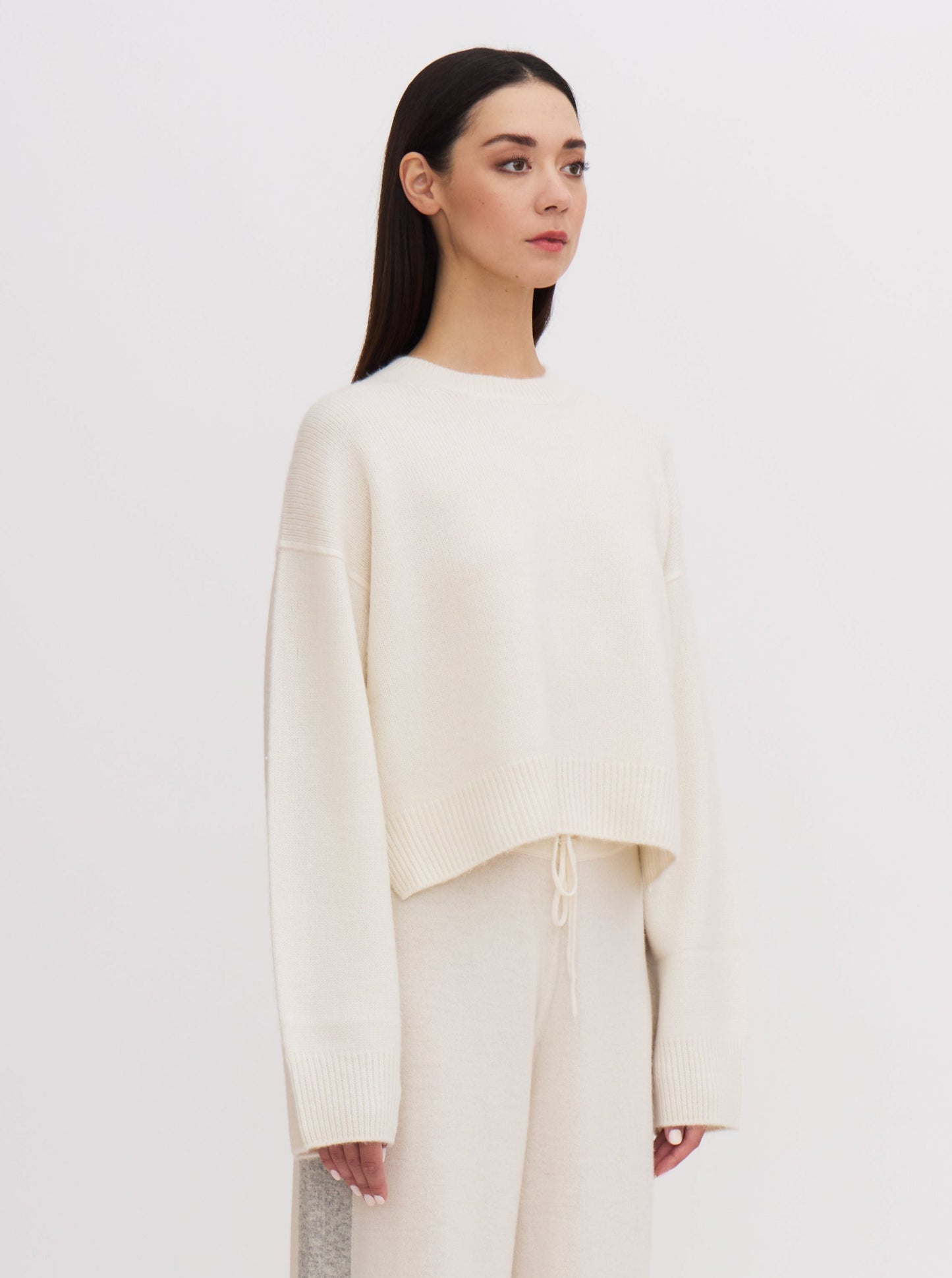 Side view of model in white short round neck cashmere sweater and white wide leg pants.