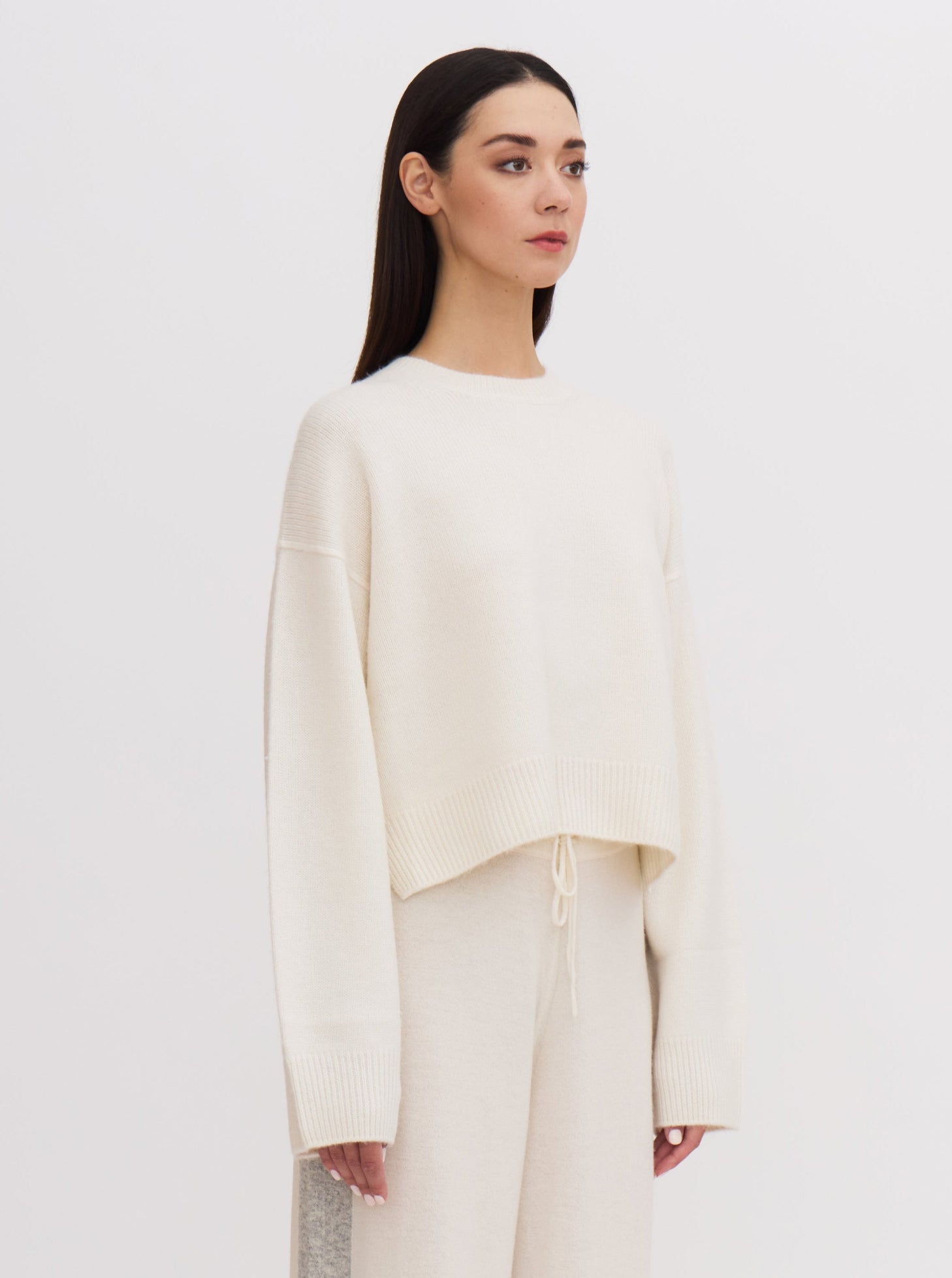 Side view of model in white short round neck cashmere sweater and white wide leg pants.