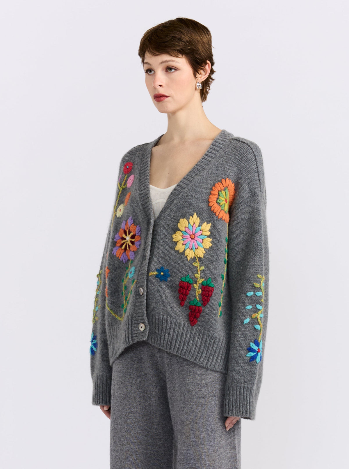 Model wearing a grey cardigan with embroidered floral patterns and matching pants on a white background