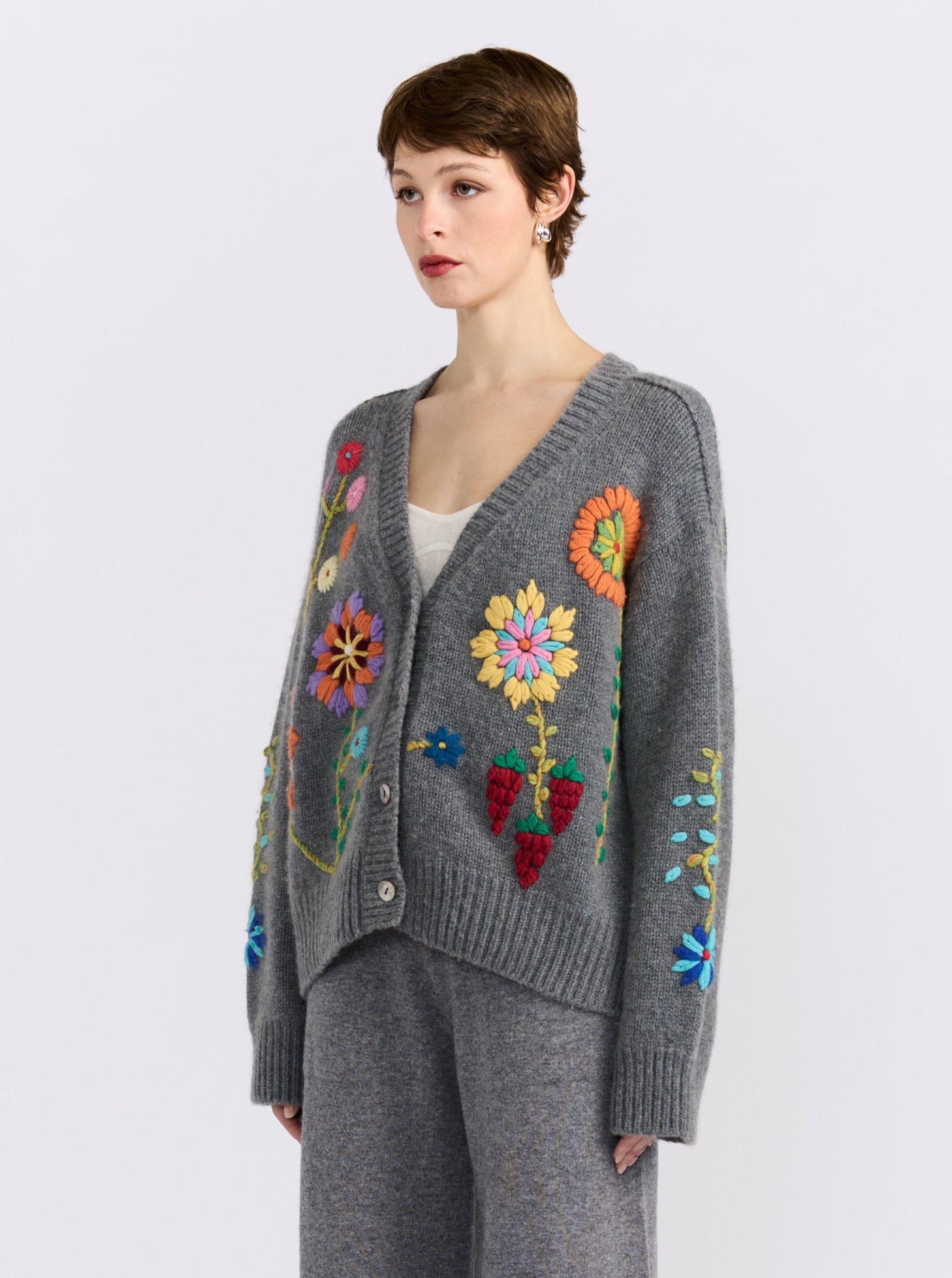 Model wearing a grey cardigan with embroidered patterns and matching pants on a white background