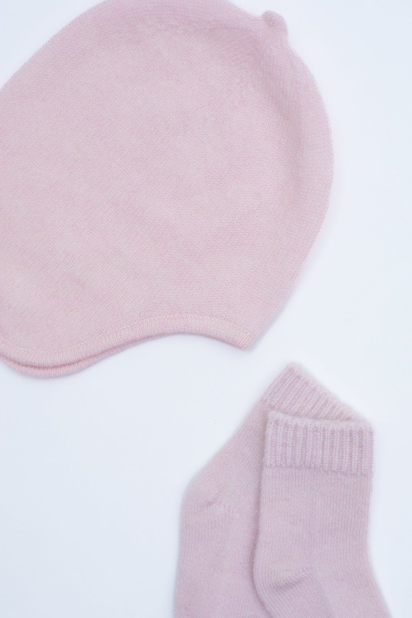 close up flat lay of the light pink cashmere baby hat and socks set 