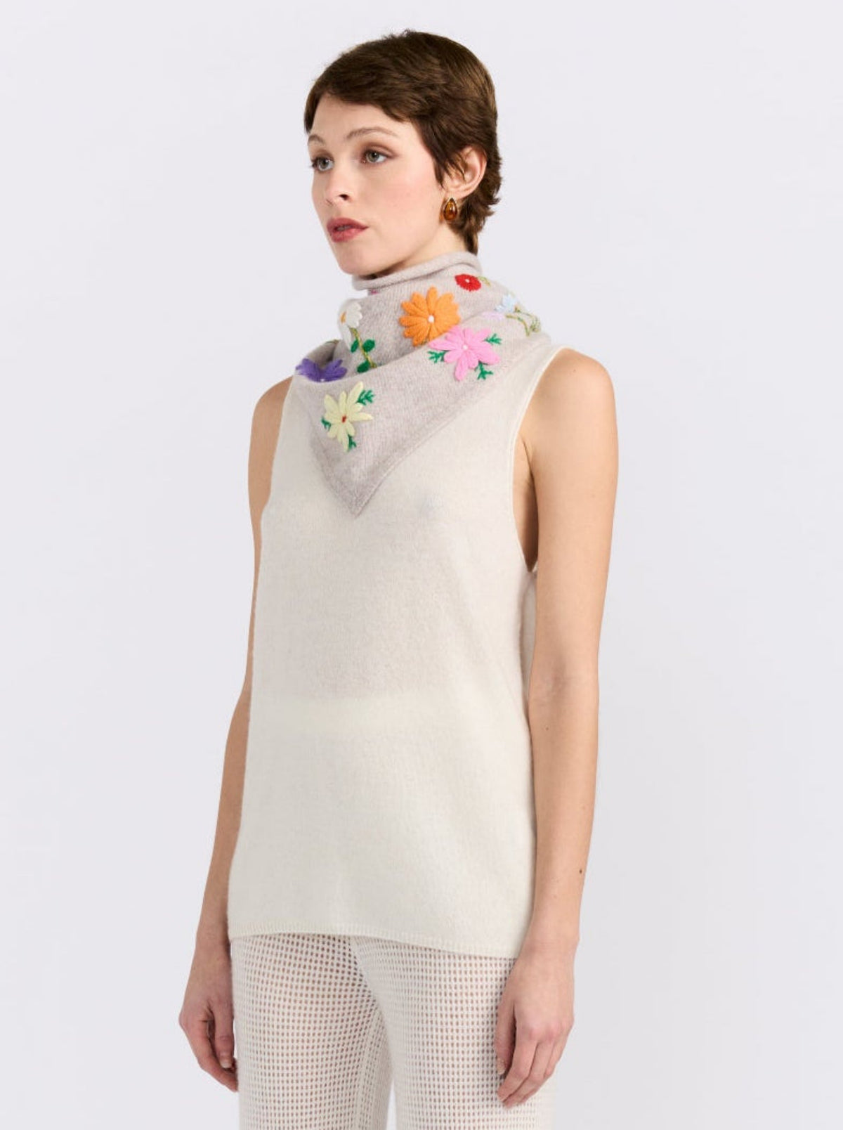 Model wearing the MANDKHAI New Beige embroidered triangle cashmere scarf styled around the neck.
